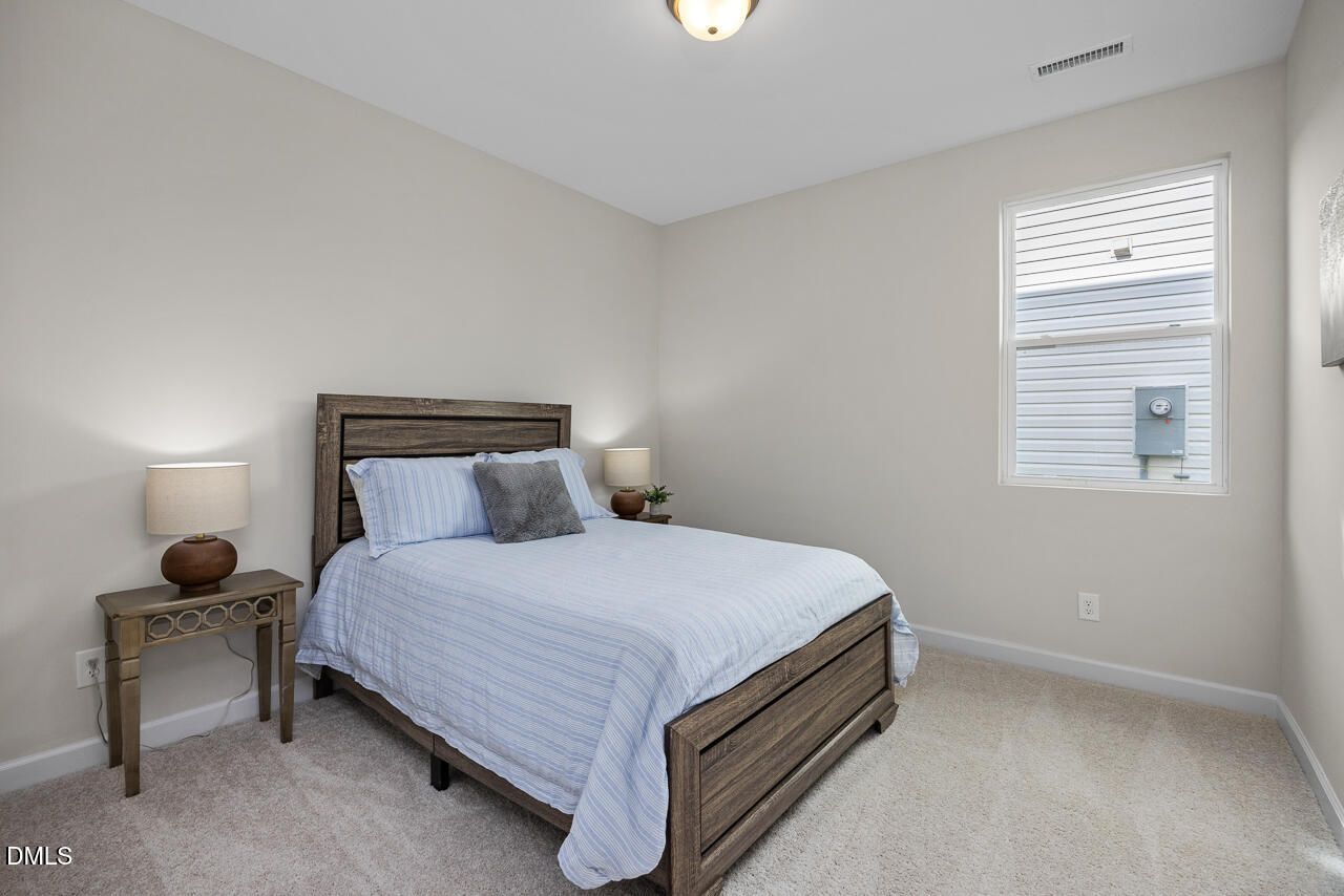 Cozy bedroom with wooden bed frame, blue plaid bedding, nightstands, and window in Davidson Homes Preston A, Lillington, NC