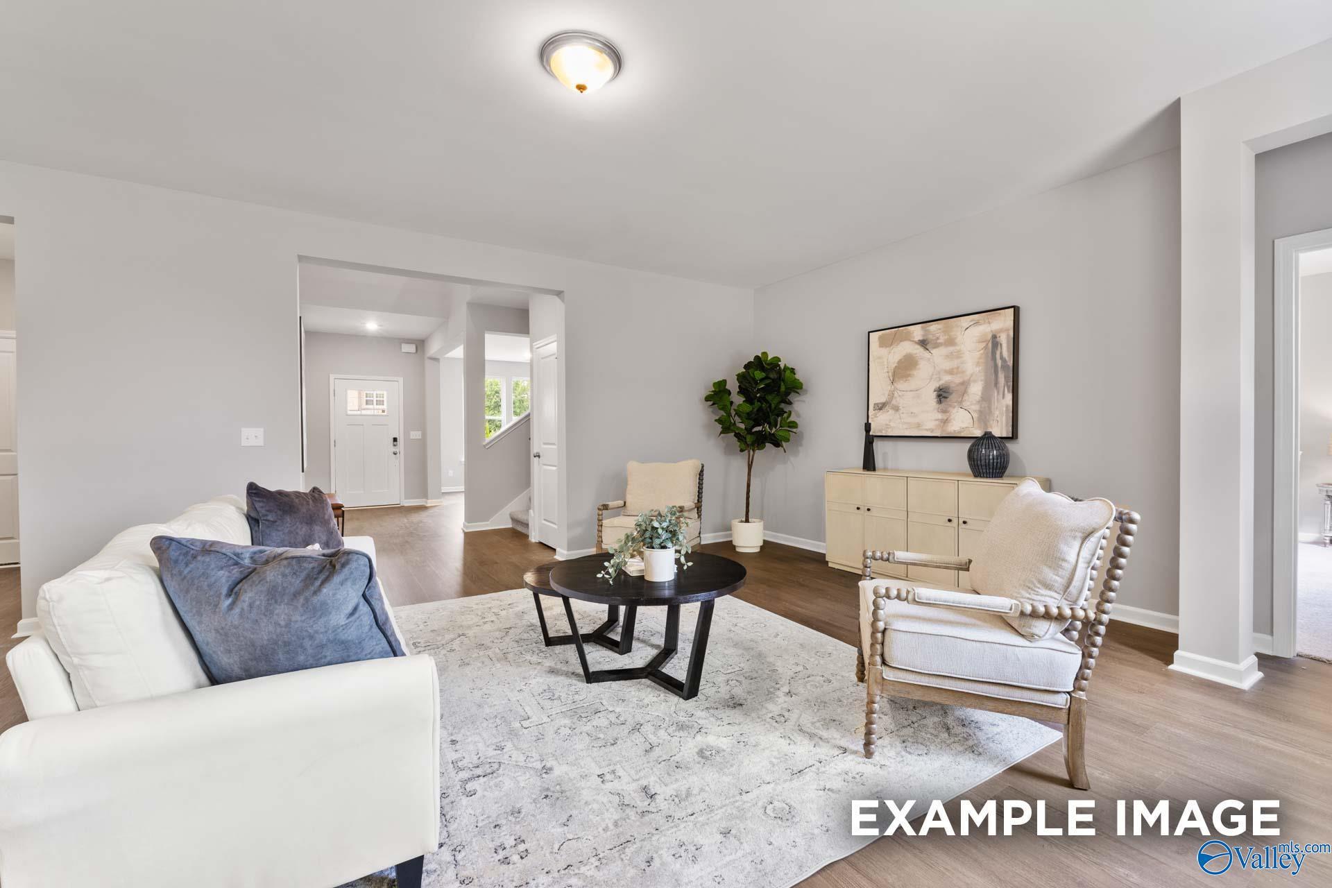 Cozy living room featuring white sofa, beige armchair, potted plants, abstract wall art in Evermore Homes The Avalon D, Owens Cross Roads, Alabama