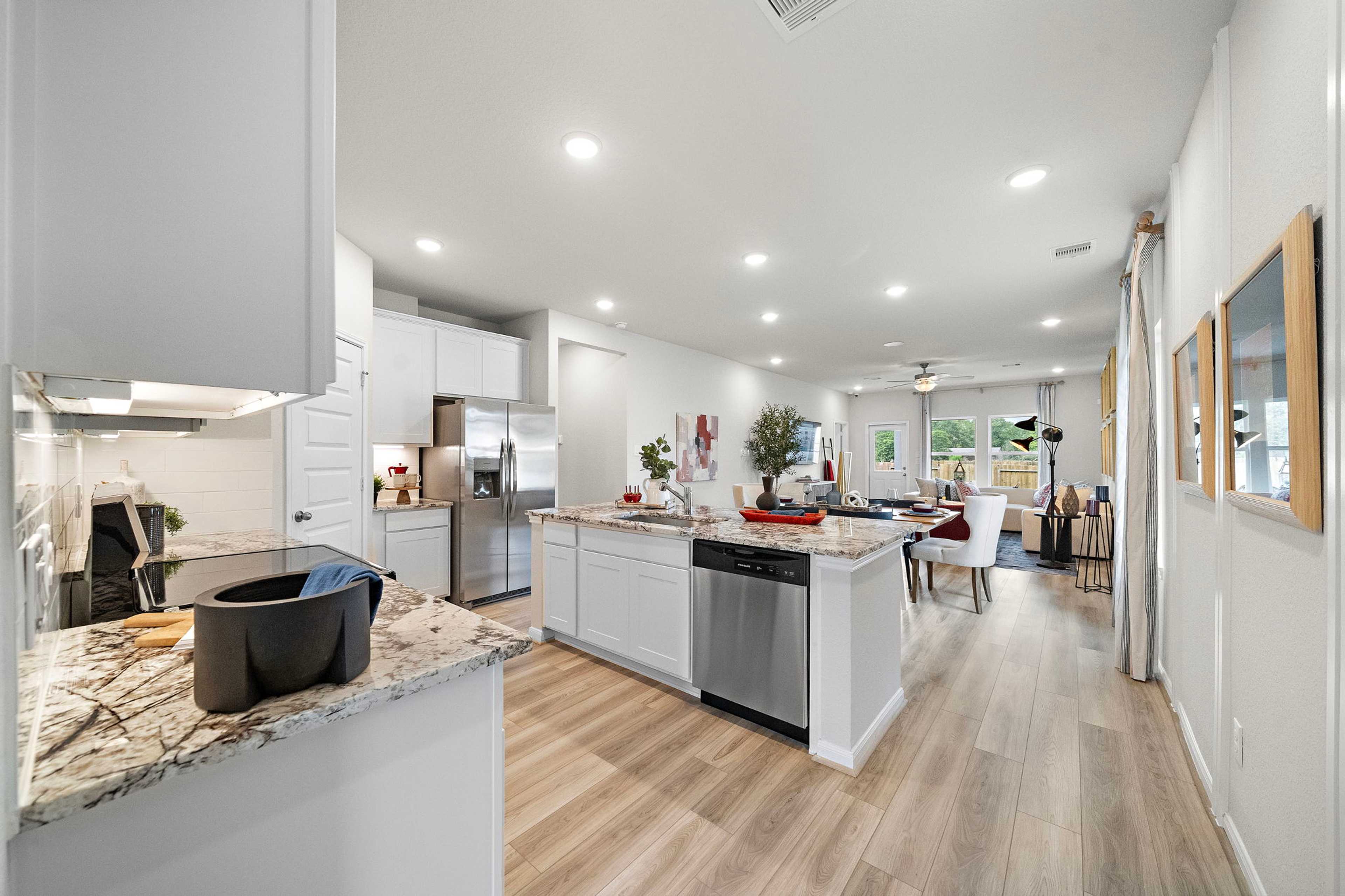 Spacious open-concept kitchen at Liberty Estates in Cleveland Texas with white shaker cabinets granite island stainless appliances and hardwood floors