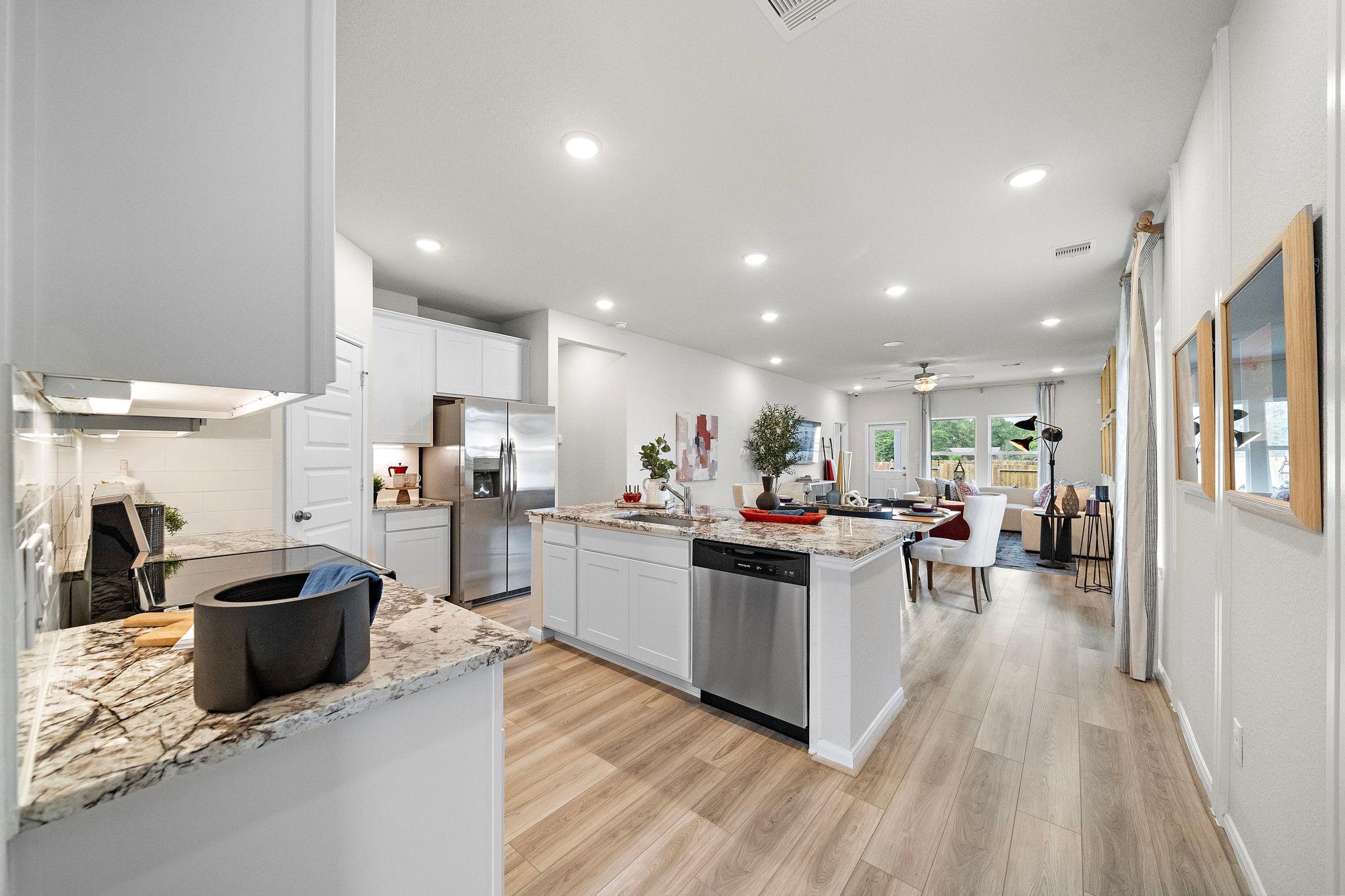 Spacious open-concept kitchen at Liberty Estates in Cleveland Texas with white shaker cabinets granite island stainless appliances and hardwood floors