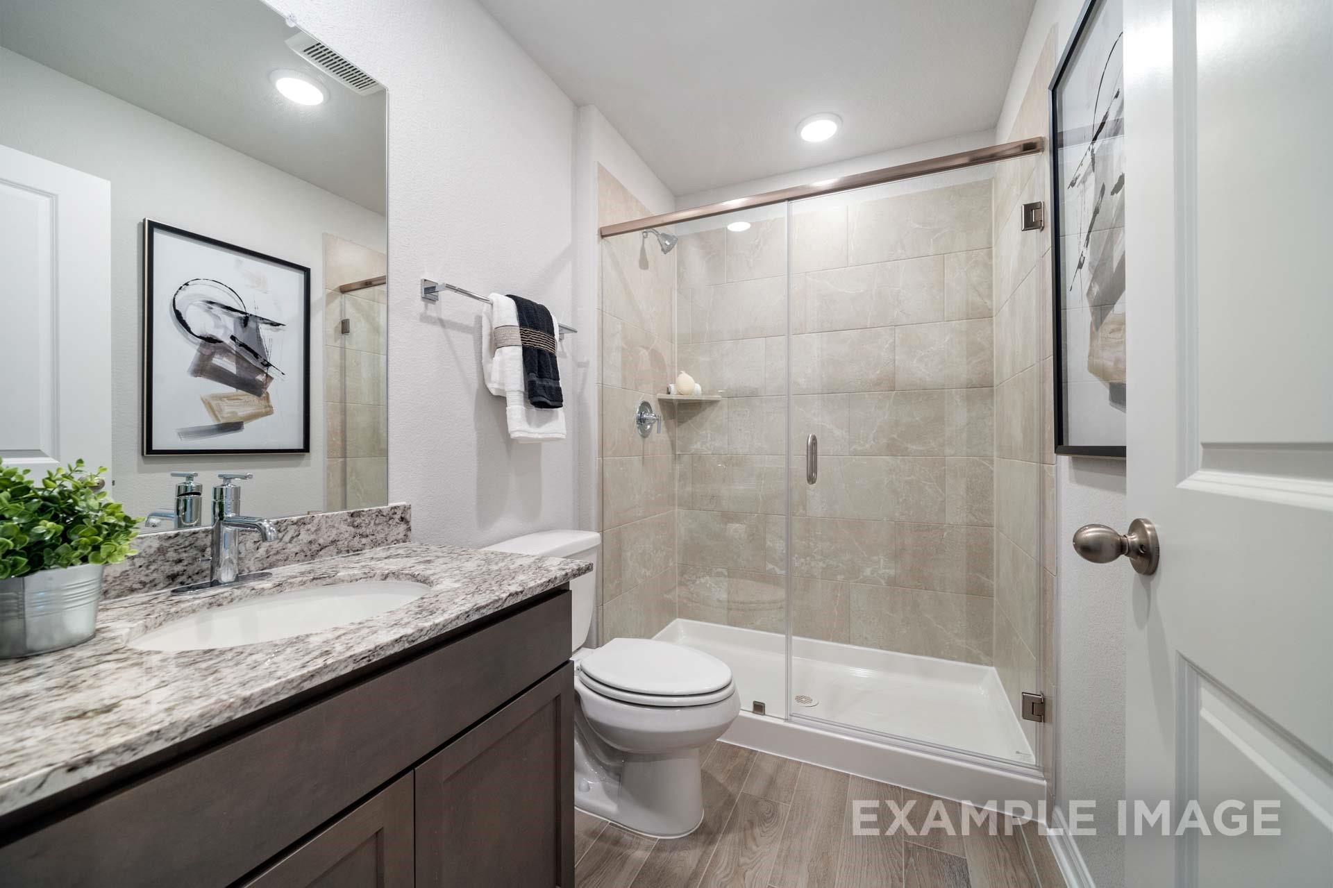 Modern bathroom with granite vanity, glass walk-in shower, and wood-look tile flooring in Davidson Homes Acadia A, Texas City