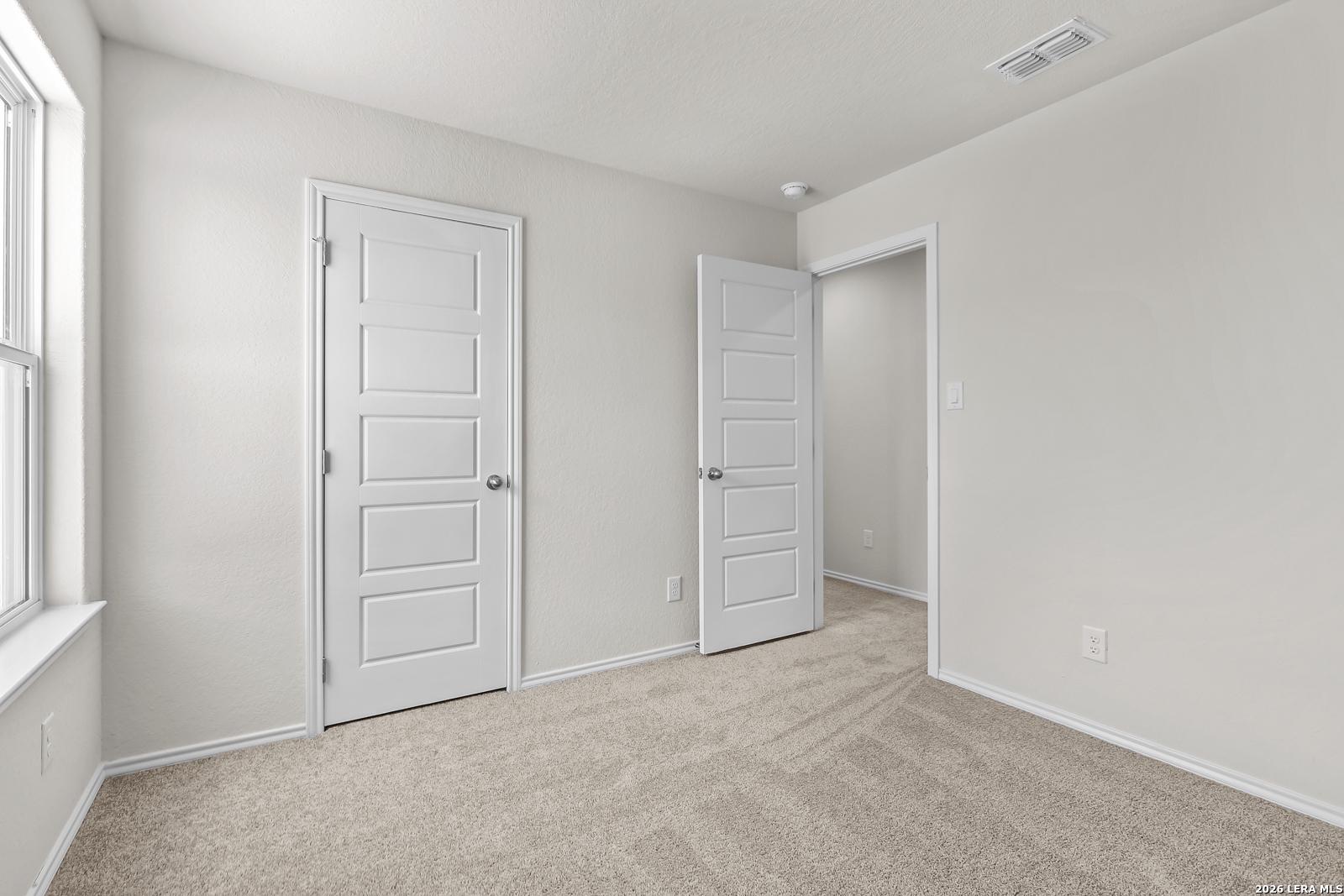 Bright bedroom with neutral carpet and closet doors in The Gillian B floor plan at Meadows at Oak Creek, San Antonio.