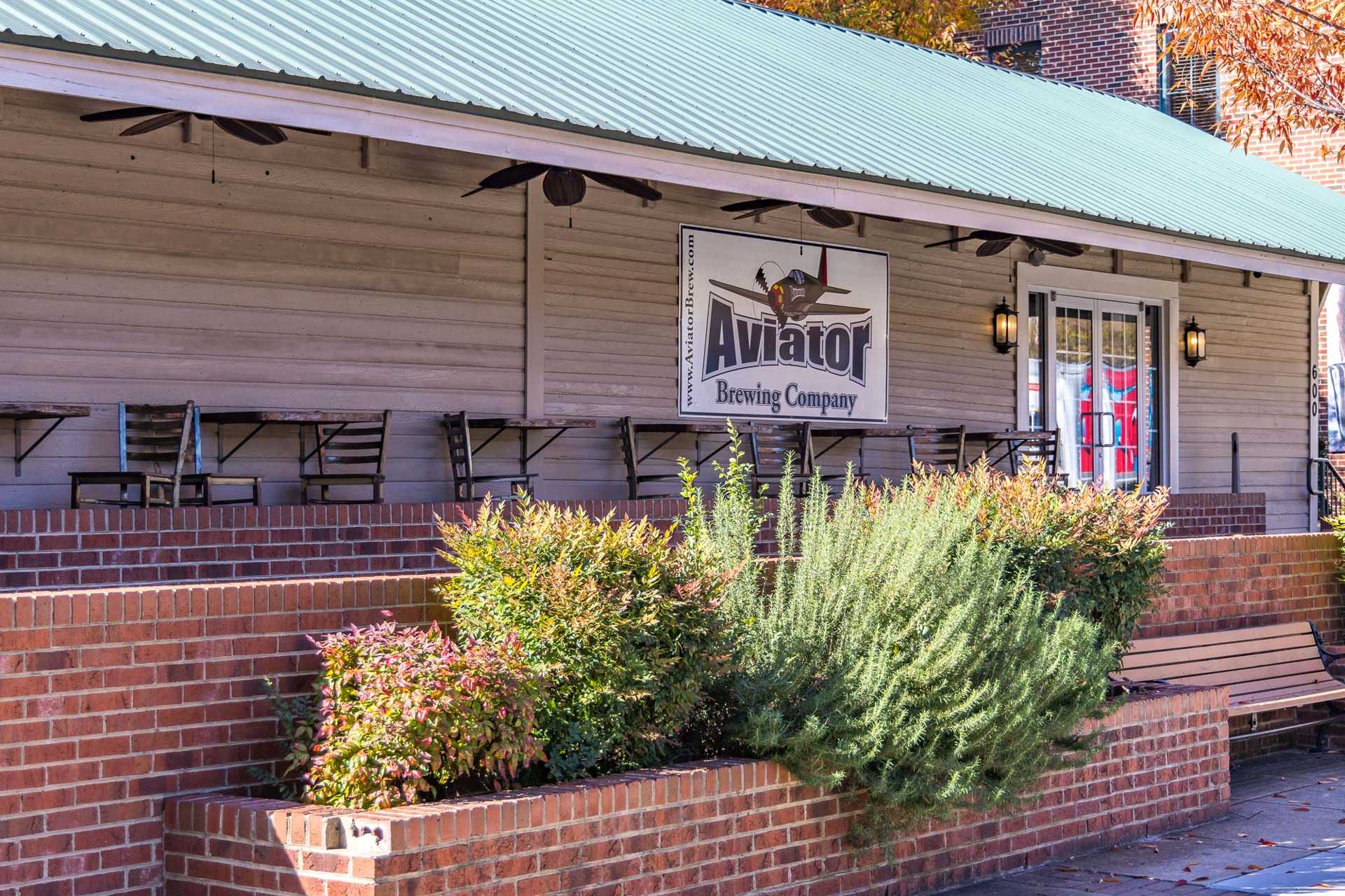Aviator Brewing Company exterior in Fuquay-Varina NC with green metal roof, wooden patio seating, brick base, and fall shrubs