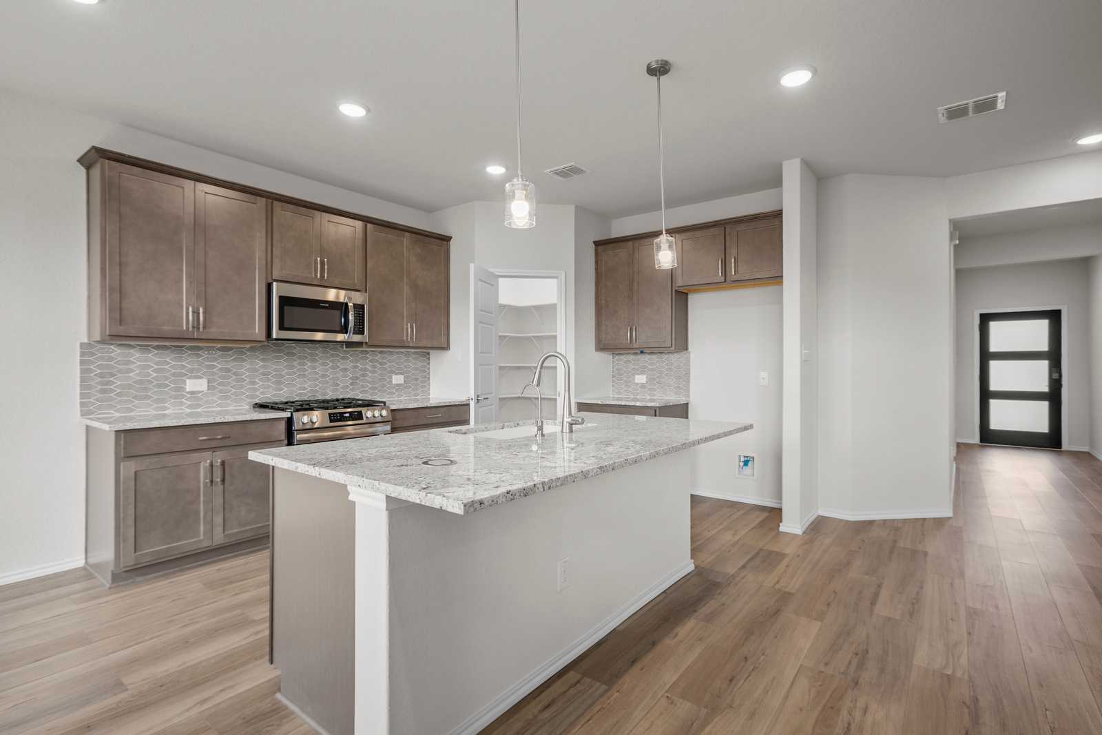 Open-concept kitchen with quartz island, stainless appliances, and shaker cabinets in Davidson Homes The Redbud B, Josephine, Texas