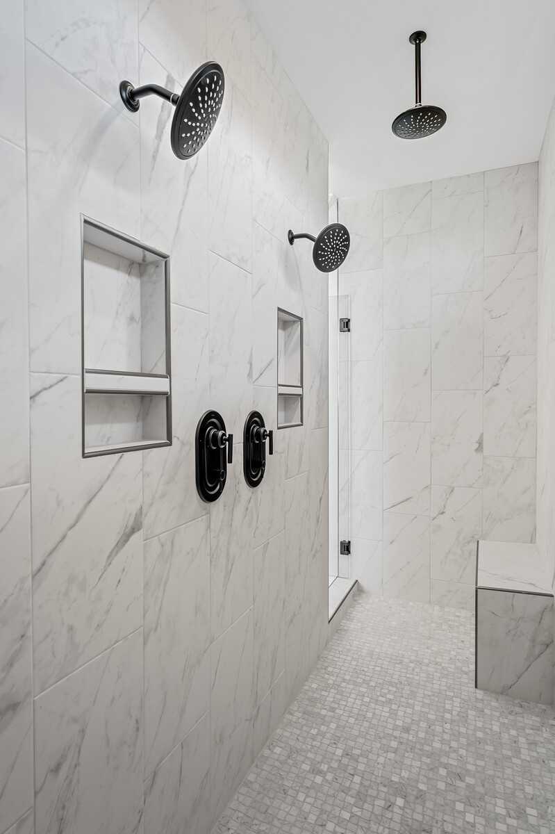 Luxurious marble-tiled walk-in shower with dual rain showerheads, niches, and bench in The Alston A master bath, Murfreesboro, TN