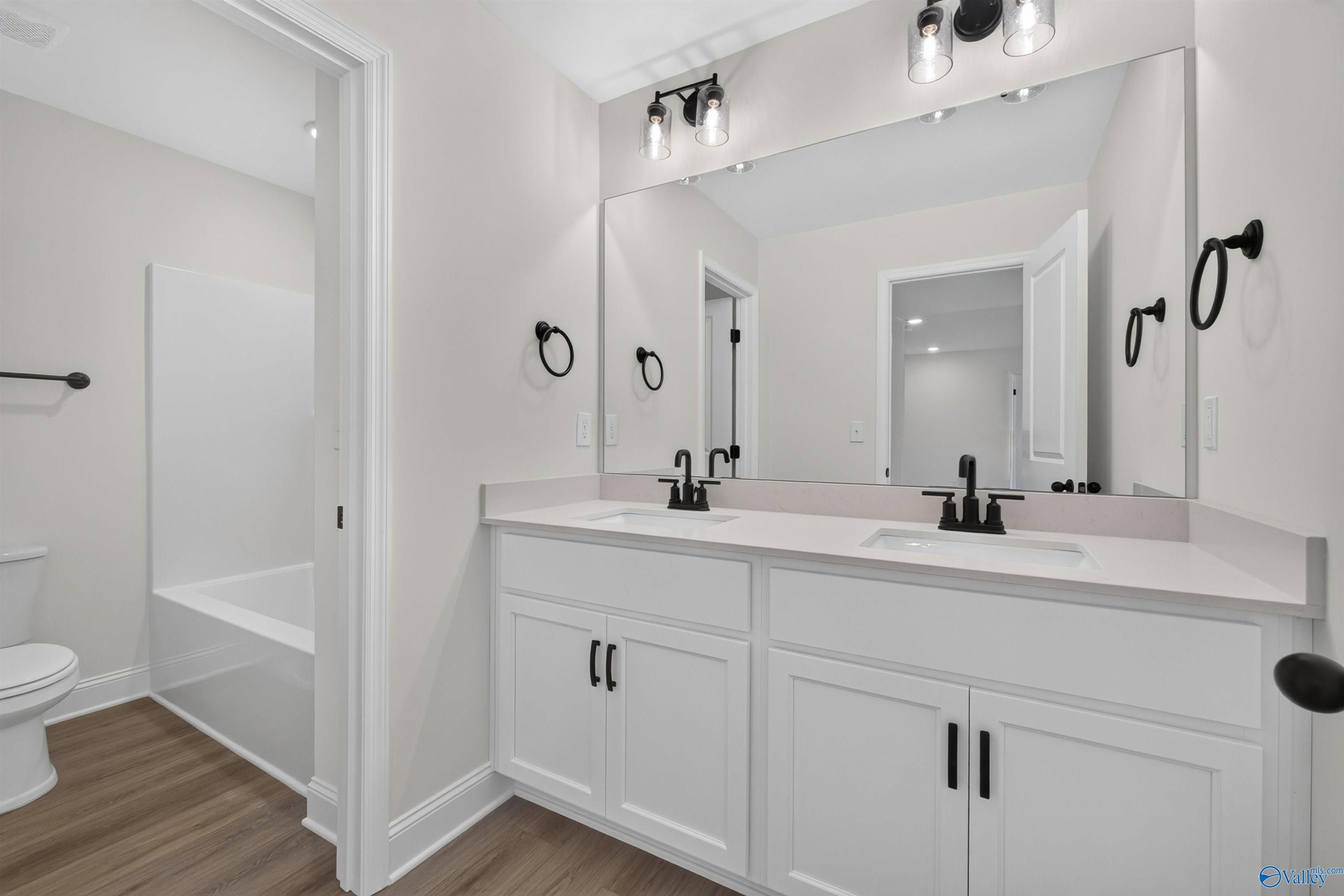 Double vanity bathroom with white shaker cabinets, matte black fixtures, and bathtub in The Ashport L, Berry Cove, New Market, Alabama