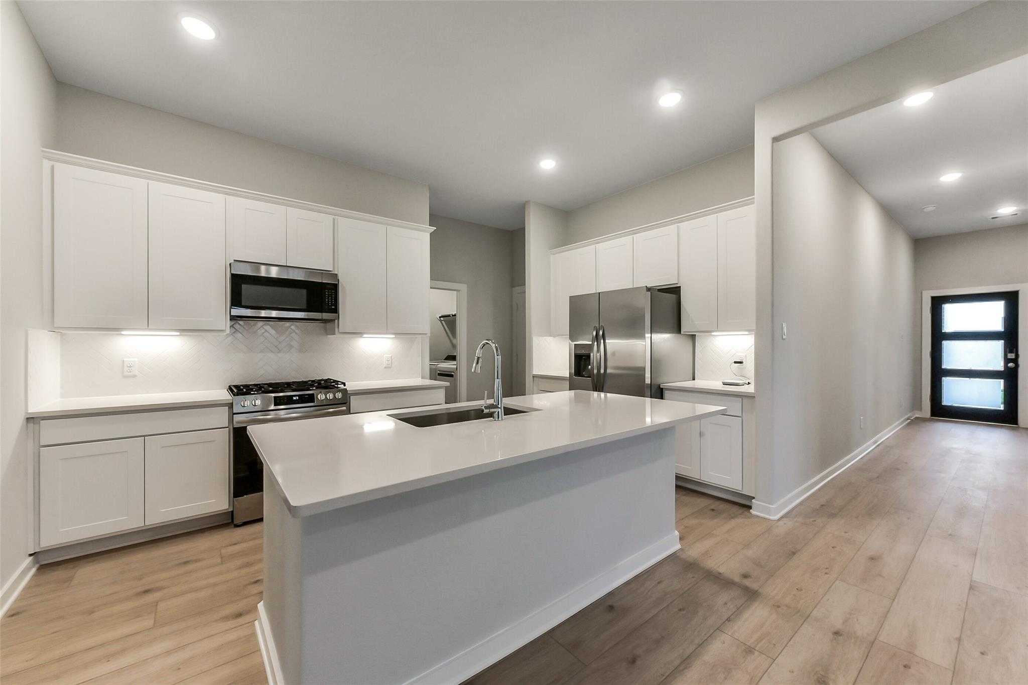 Modern white kitchen with stainless appliances, quartz island sink, and open layout in Davidson Homes The Laguna B, Katy, Texas