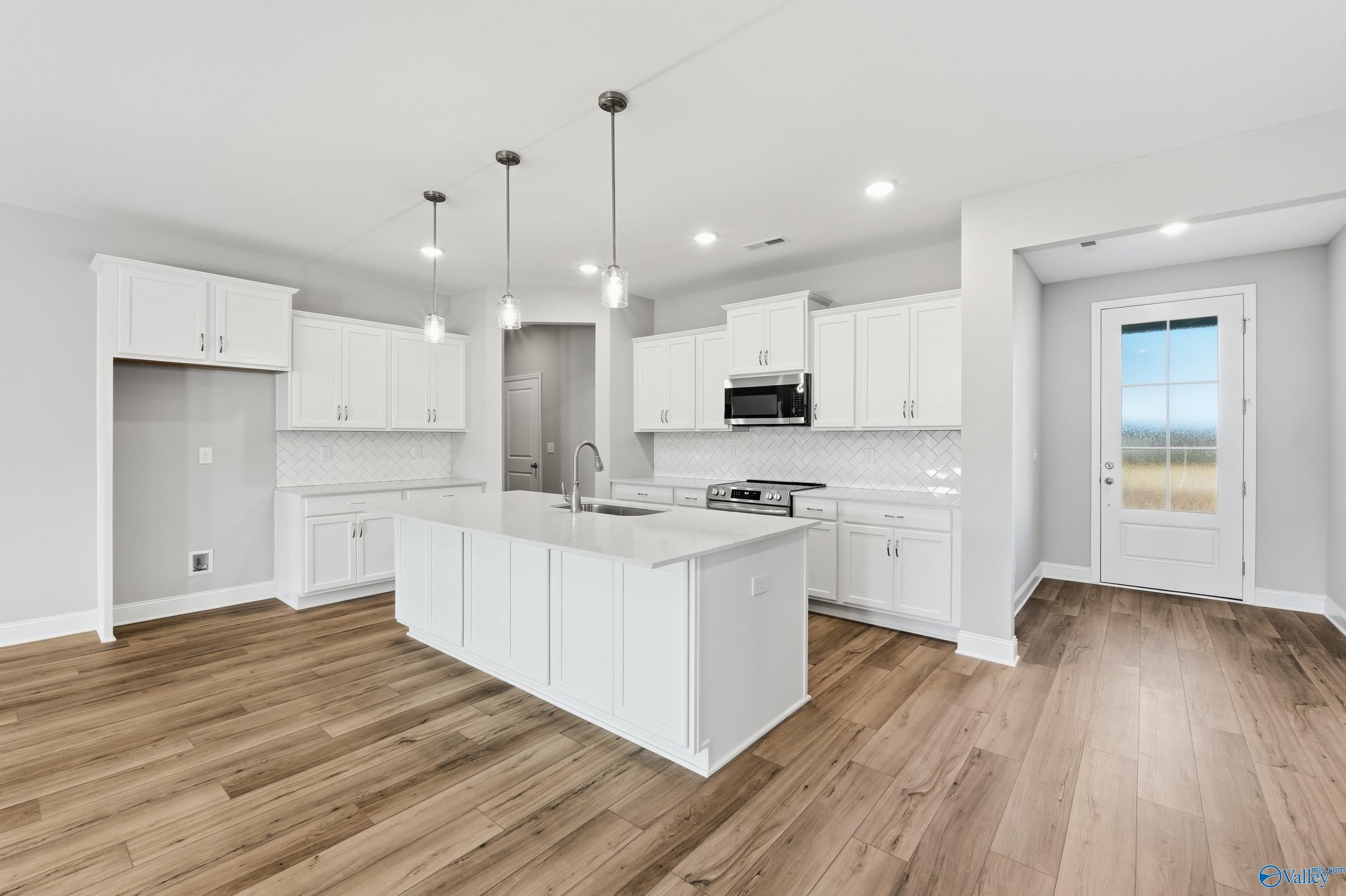 Modern white kitchen with large island, stainless appliances, pendant lights, and hardwood floors in The Lanier plan, Toney, Alabama