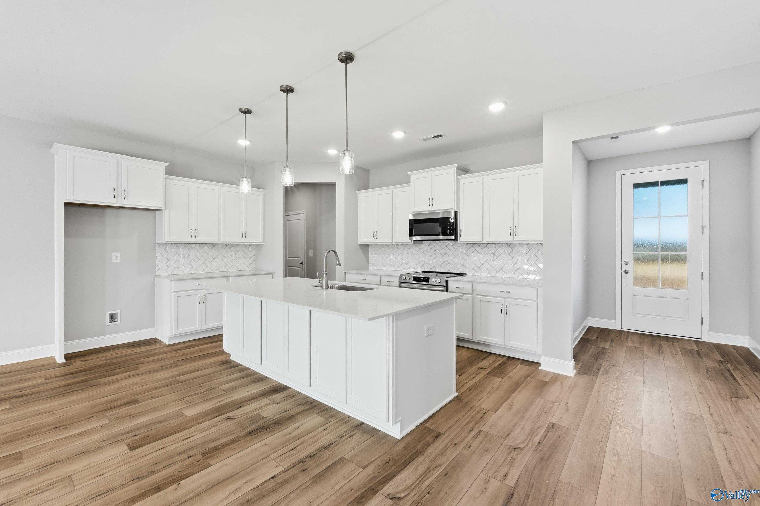 Modern white kitchen with large island, stainless appliances, pendant lights, and hardwood floors in The Lanier plan, Toney, Alabama