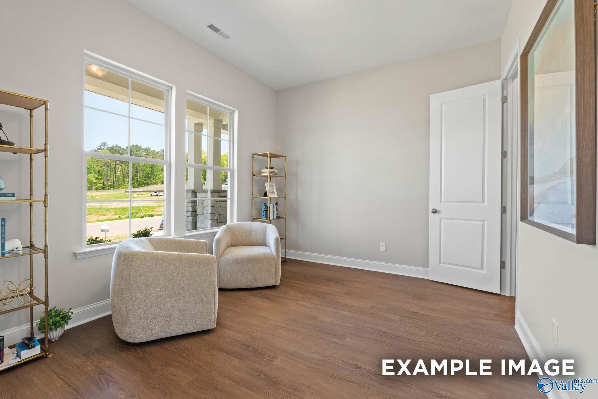 Cozy study room with large windows overlooking trees, beige armchairs, gold bookshelves in Evermore Homes The Haven E, Owens Cross Roads, AL