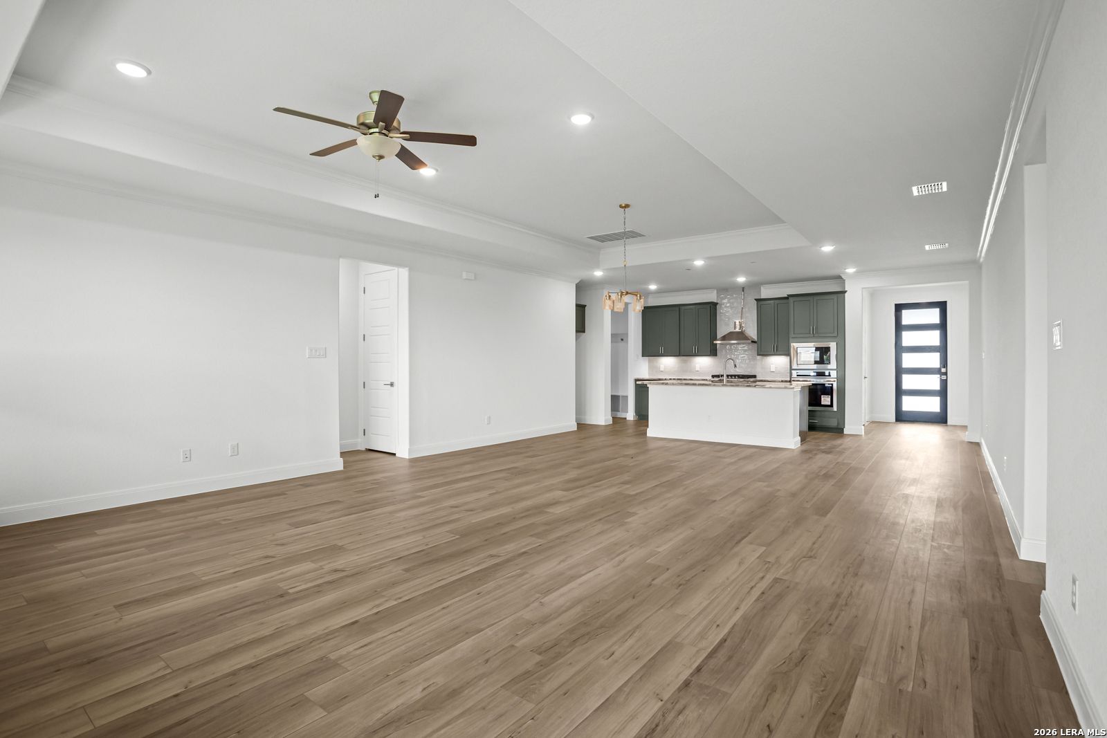 Open-concept living room and kitchen with wood flooring in The Lanier G floor plan at The Reserve at Potranco Oaks.