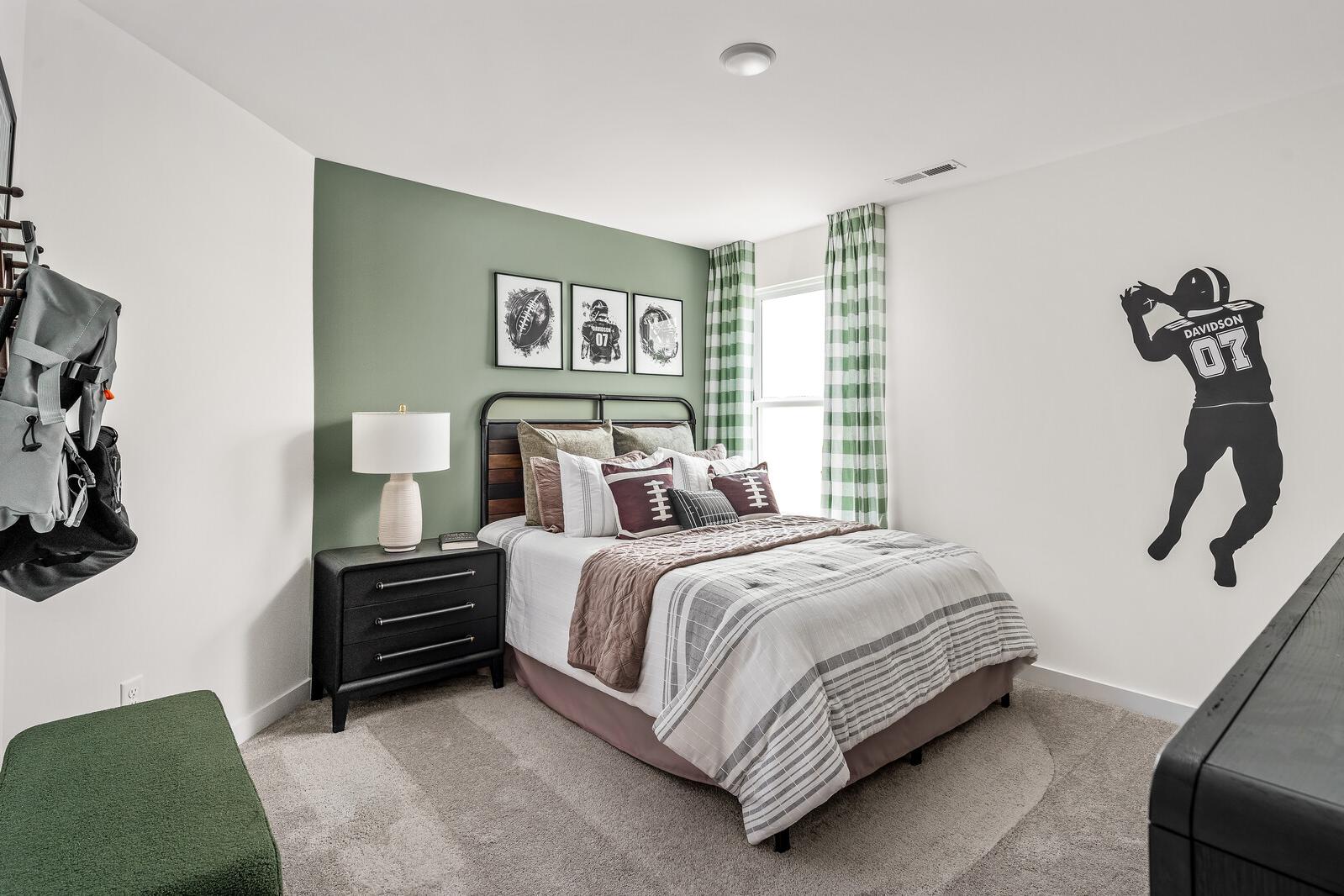 Sports-themed bedroom at Woods Crossing in Gallatin Tennessee with green accent wall, queen bed, football player silhouette, and checkered curtains