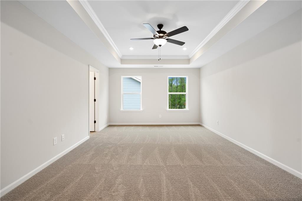 Empty bedroom with tray ceiling, ceiling fan, and large windows in Davidson Homes The Marion A, Kennesaw, Georgia