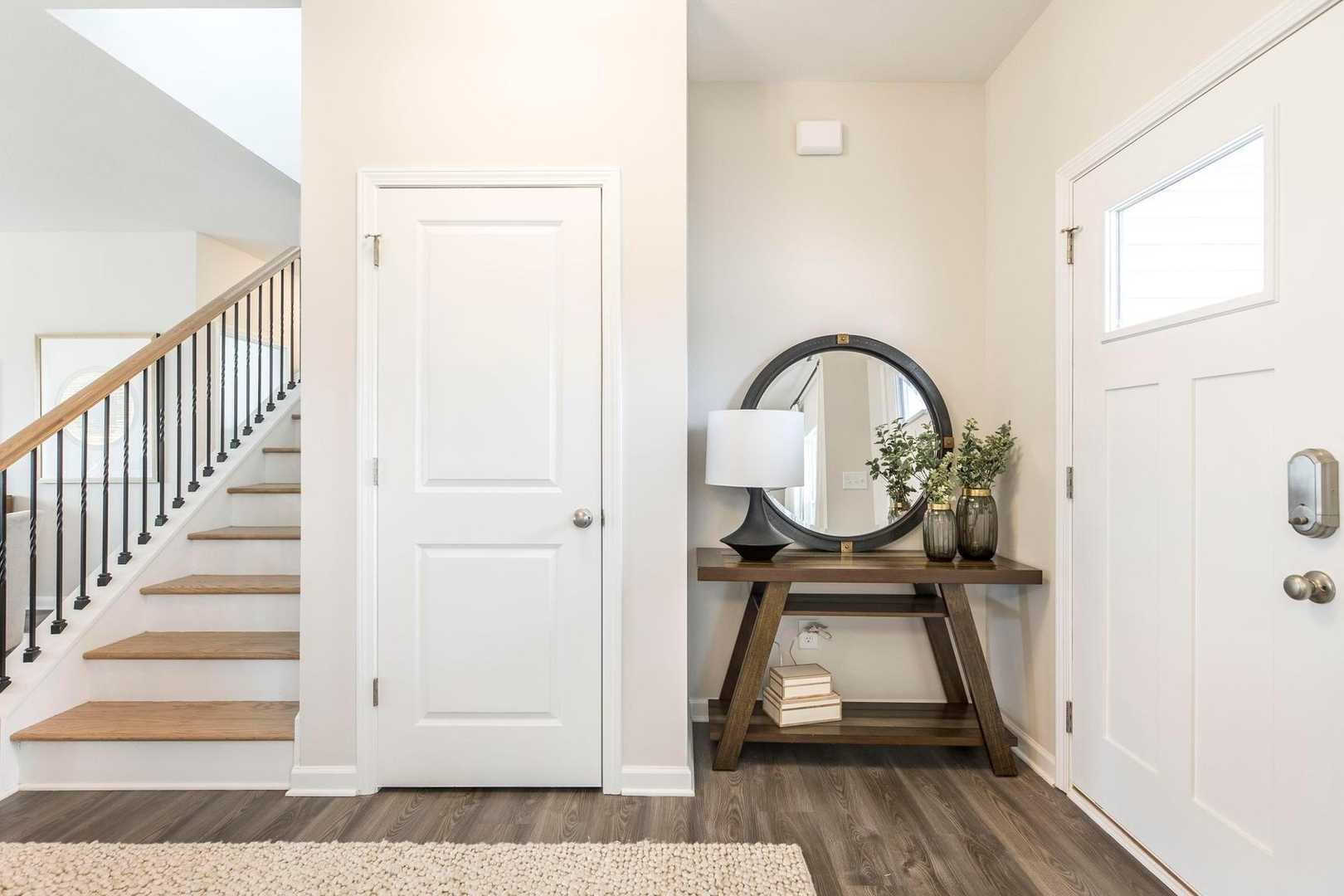 Bright entry foyer at Cape Reserve Donahue Ridge Auburn AL with oak staircase hardwood floors and console table mirror lamp