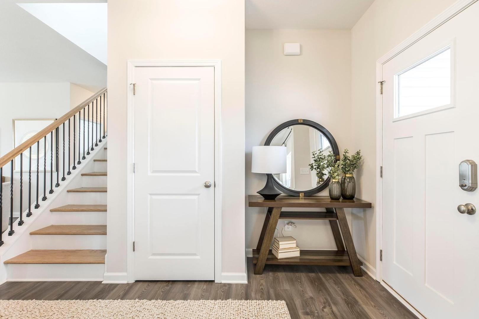 Bright entry foyer at Cape Reserve Donahue Ridge Auburn AL with oak staircase hardwood floors and console table mirror lamp