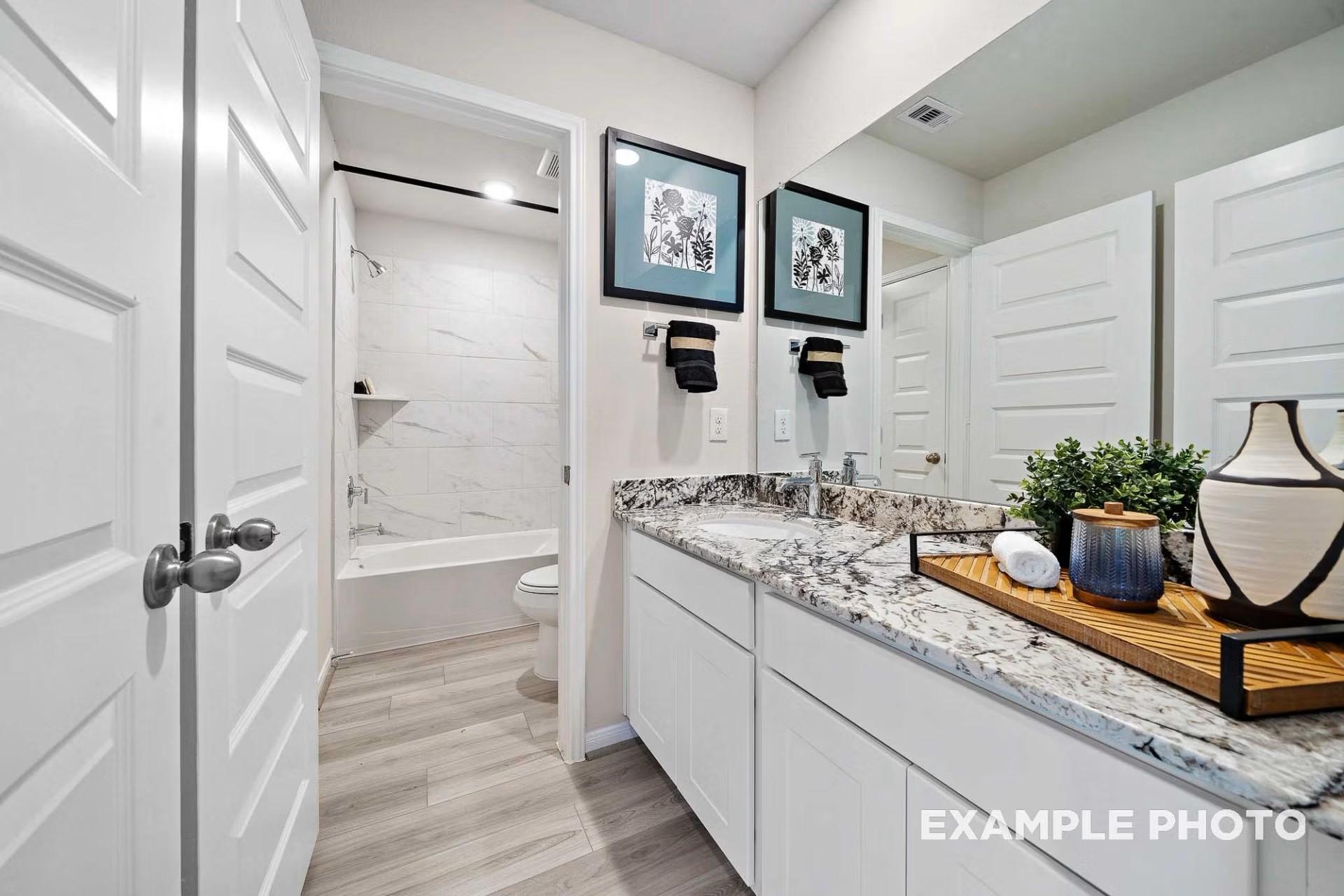 Modern bathroom with granite vanity, white cabinets, and tile shower in Davidson Homes The San Marcos E in Heartland, Texas.