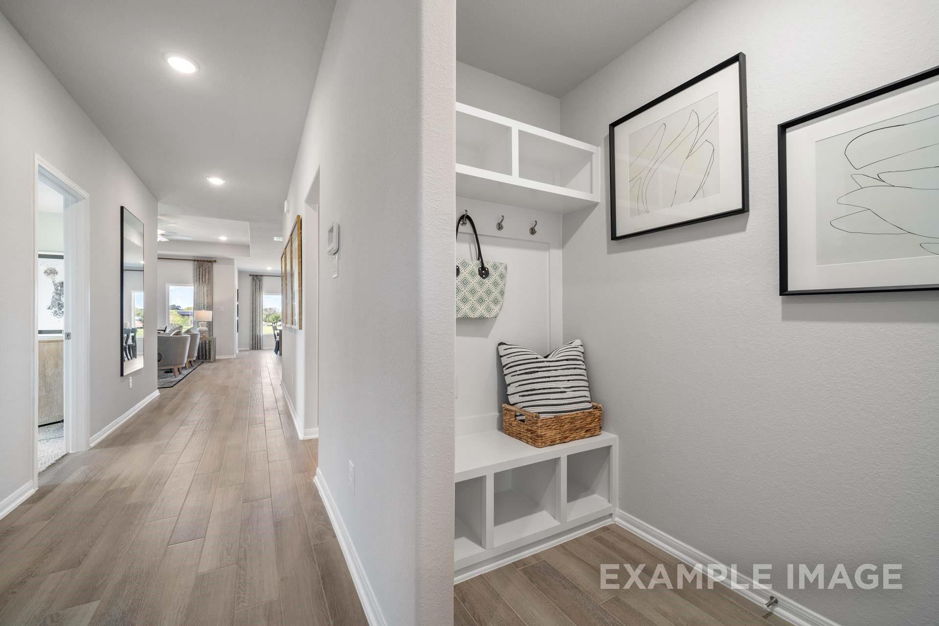 Mudroom with built-in bench, cubbies, and coat hooks beside wood-look tile hallway in Davidson Homes Acadia A, Texas City