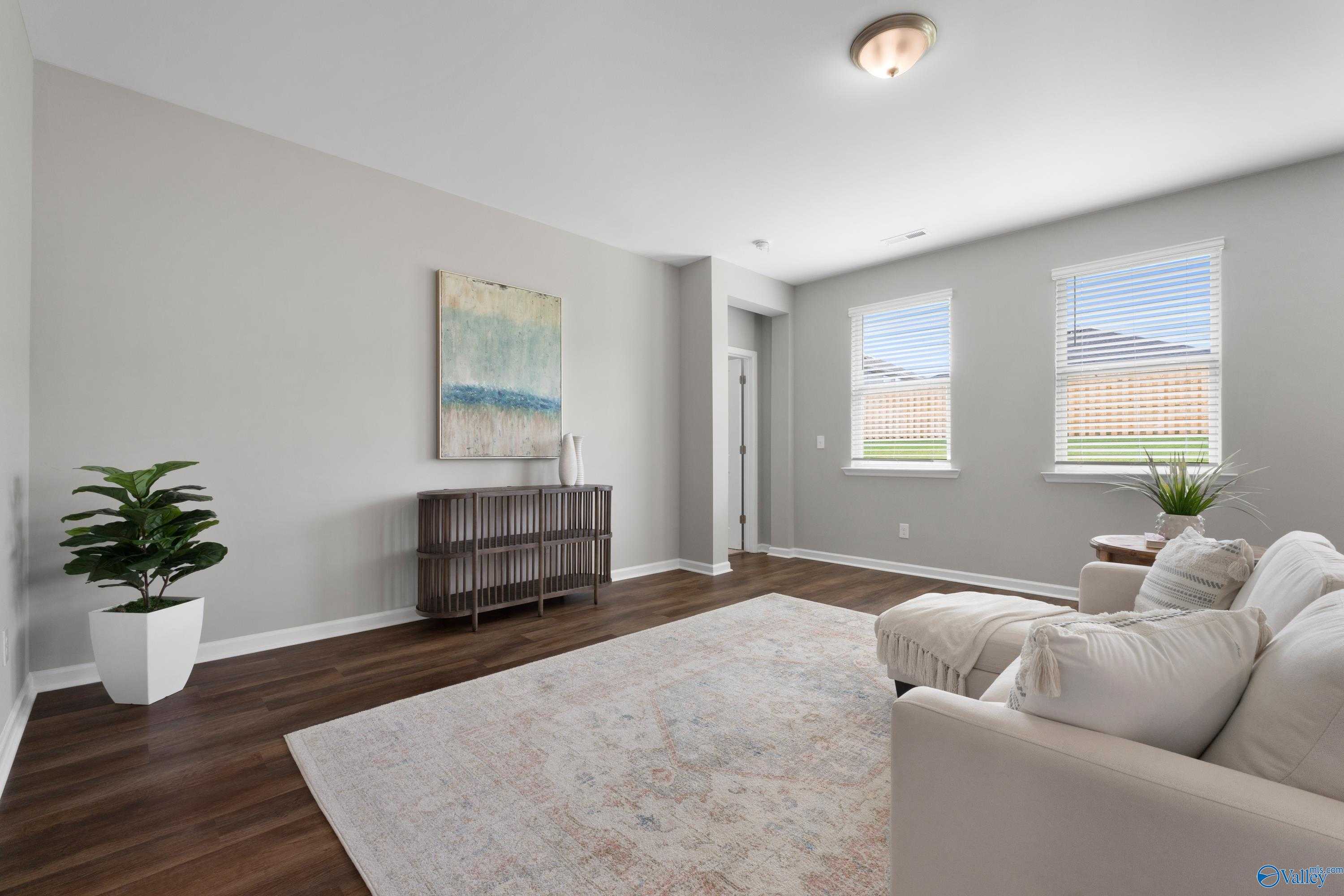 Cozy living room with white sofa, area rug, potted ferns, abstract art, and large windows in The Noble 3-bedroom home by Evermore Homes, Madison, Alabama