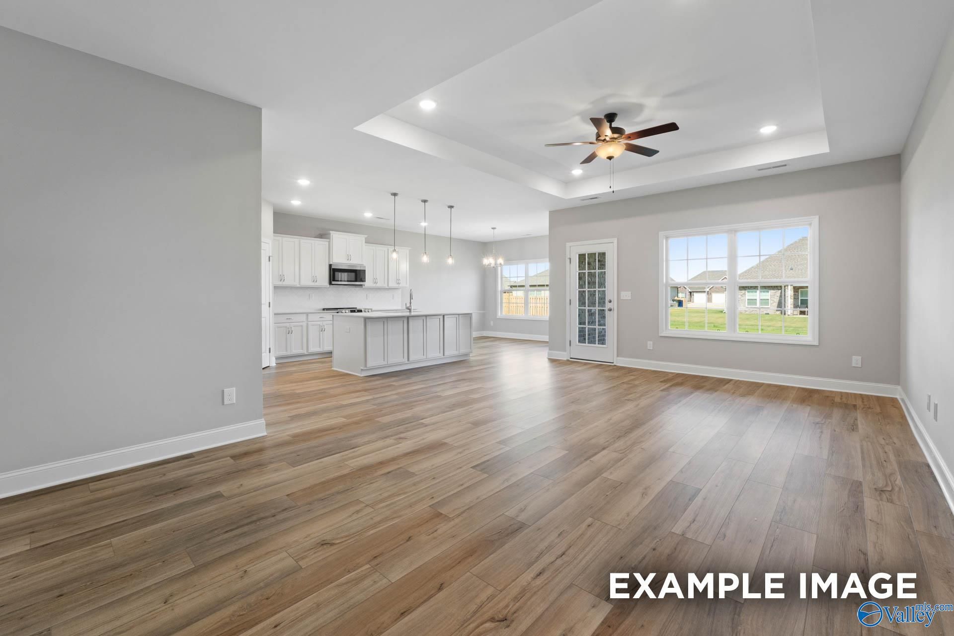 Open-concept living-kitchen with white cabinets, large island, ceiling fan, and backyard view in Davidson Homes Montgomery B, Hartselle AL