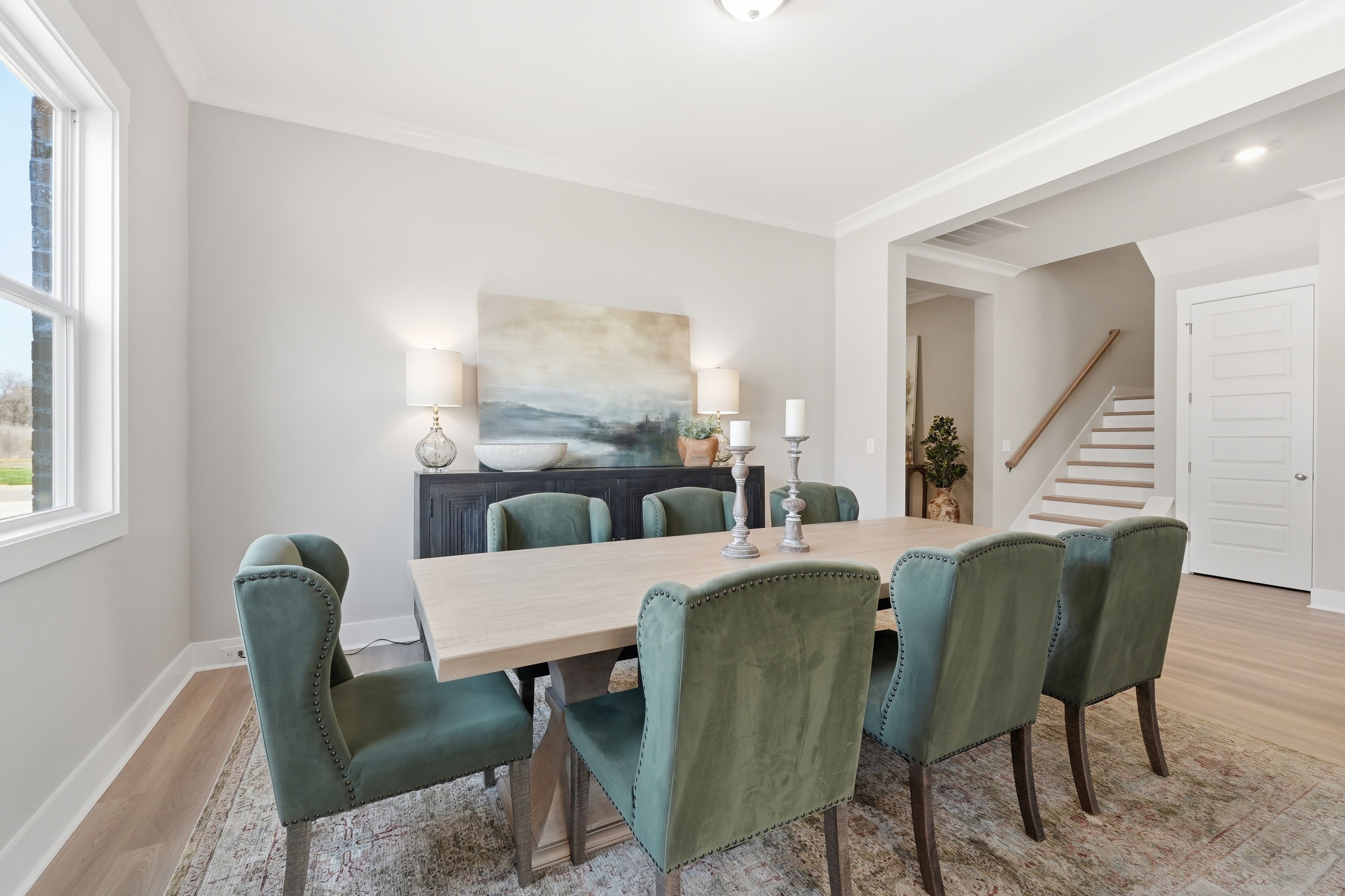Elegant dining room at The Meadows at Hampton Cove in Owens Cross Roads AL with rectangular wooden table, green velvet chairs, abstract painting, and hardwood floors
