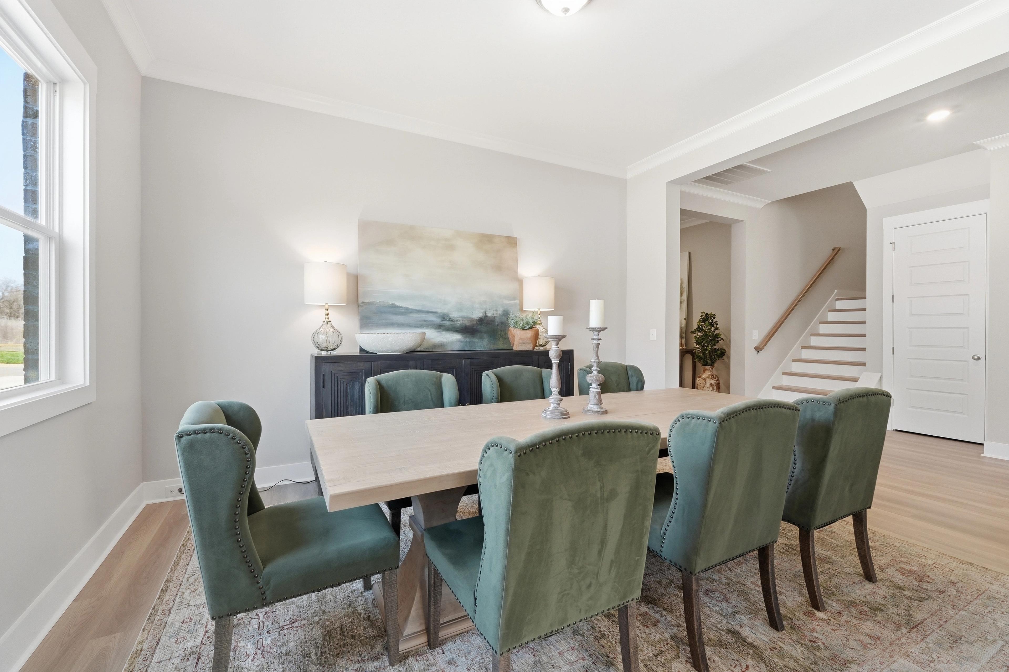 Elegant dining room at The Meadows at Hampton Cove in Owens Cross Roads AL with rectangular wooden table, green velvet chairs, abstract painting, and hardwood floors