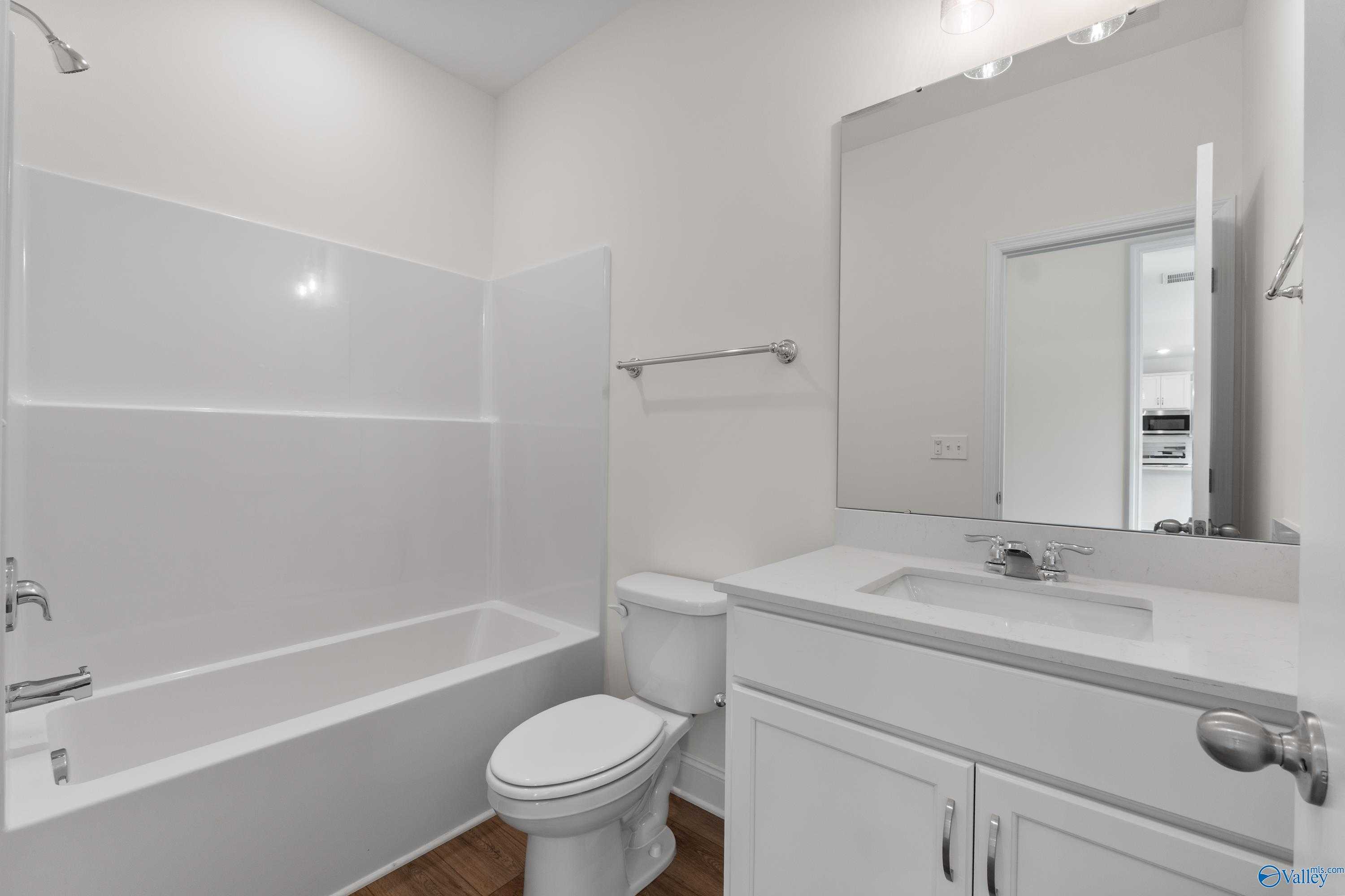 Bright bathroom with white tub-shower combo, vanity, toilet, and mirror in Davidson Homes Shelby A, New Market, Alabama