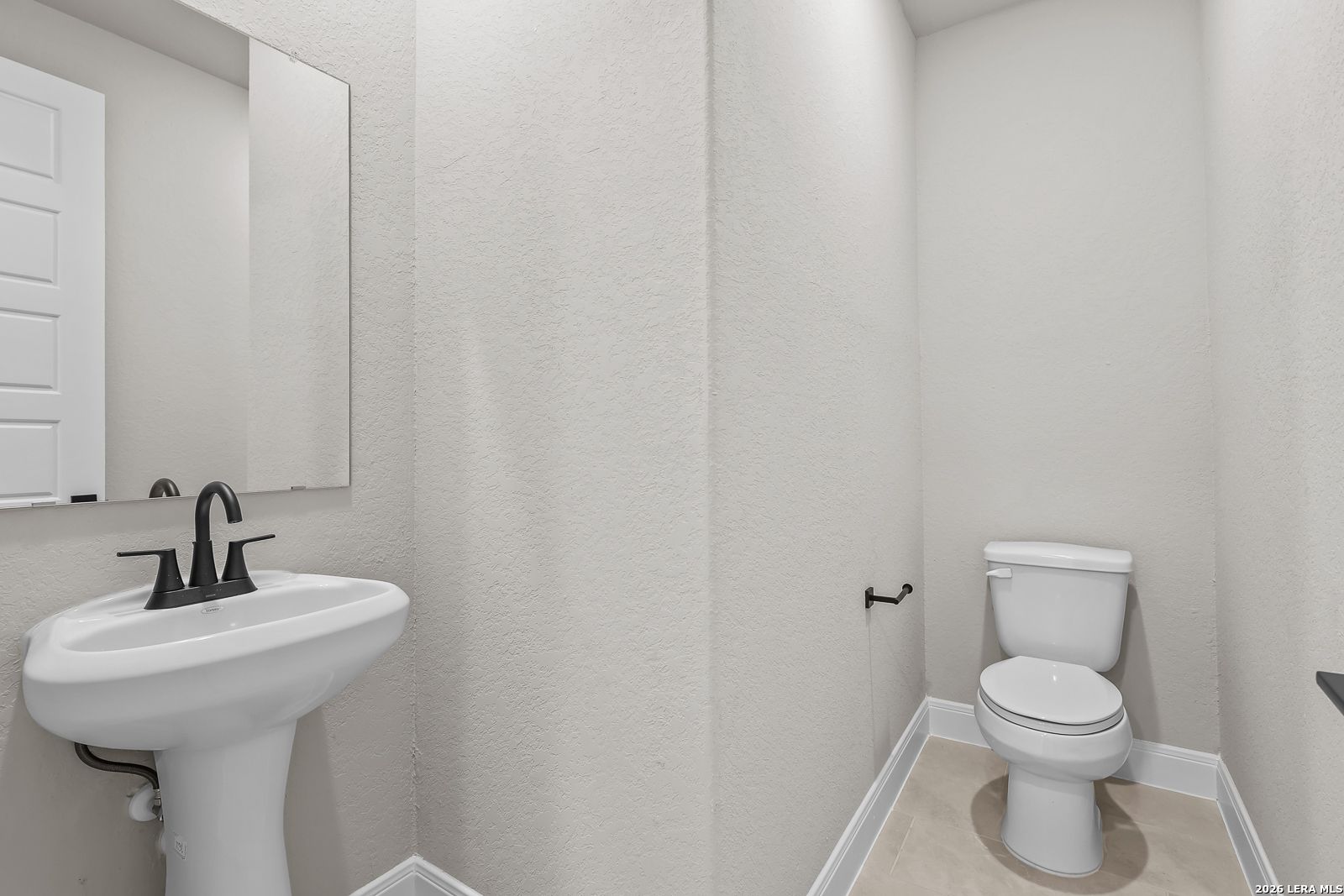 Half bath with white pedestal sink, matte black faucet, and toilet in Davidson Homes The Foster E, Potranco Oaks, Castroville, Texas