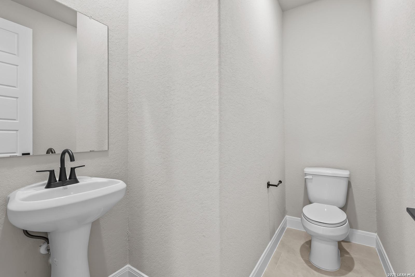 Half bath with white pedestal sink, matte black faucet, and toilet in Davidson Homes The Foster E, Potranco Oaks, Castroville, Texas