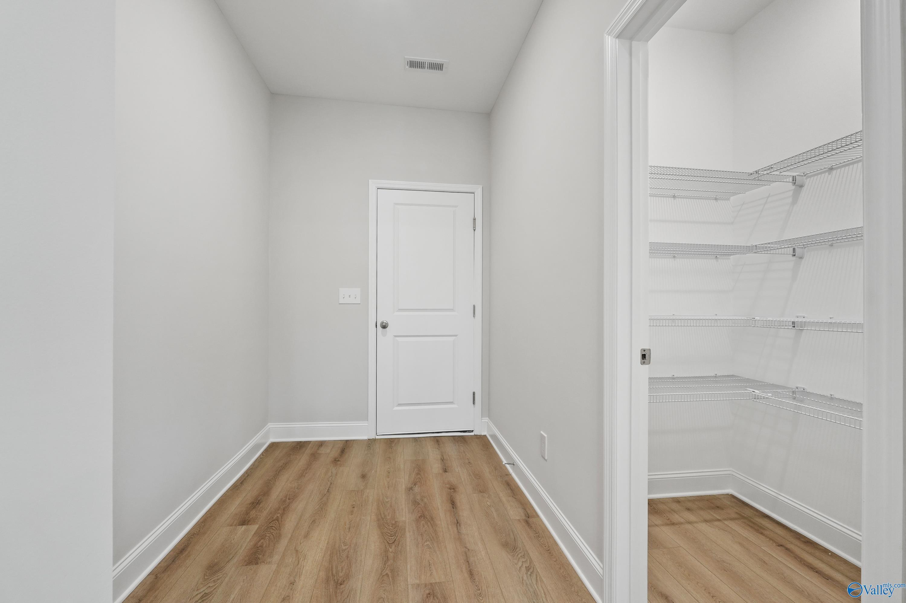 Bright bedroom with walk-in closet, wire shelving, light wood floors in Davidson Homes The Camden, Huntsville, Alabama