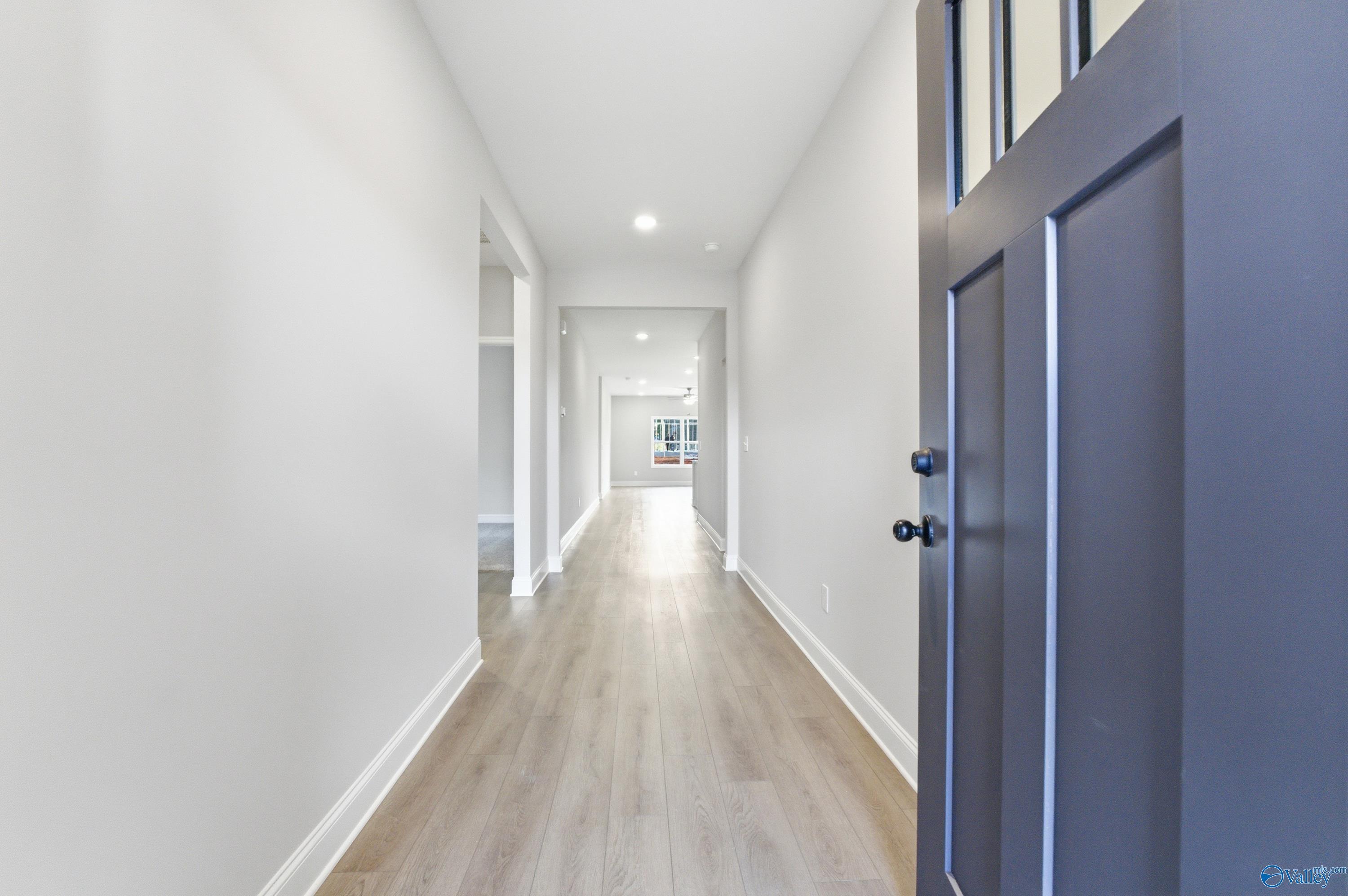 Bright hallway with light oak floors, white walls, and open doorways in Davidson Homes The Daphne C, Huntsville, AL