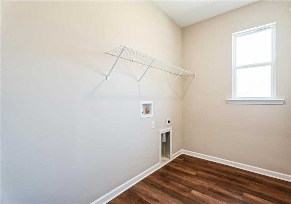 Bright laundry room with utility sink, dryer outlet, folding wall shelf, wood flooring, and window in Evermore Homes The Aurora A, Cusseta, Alabama