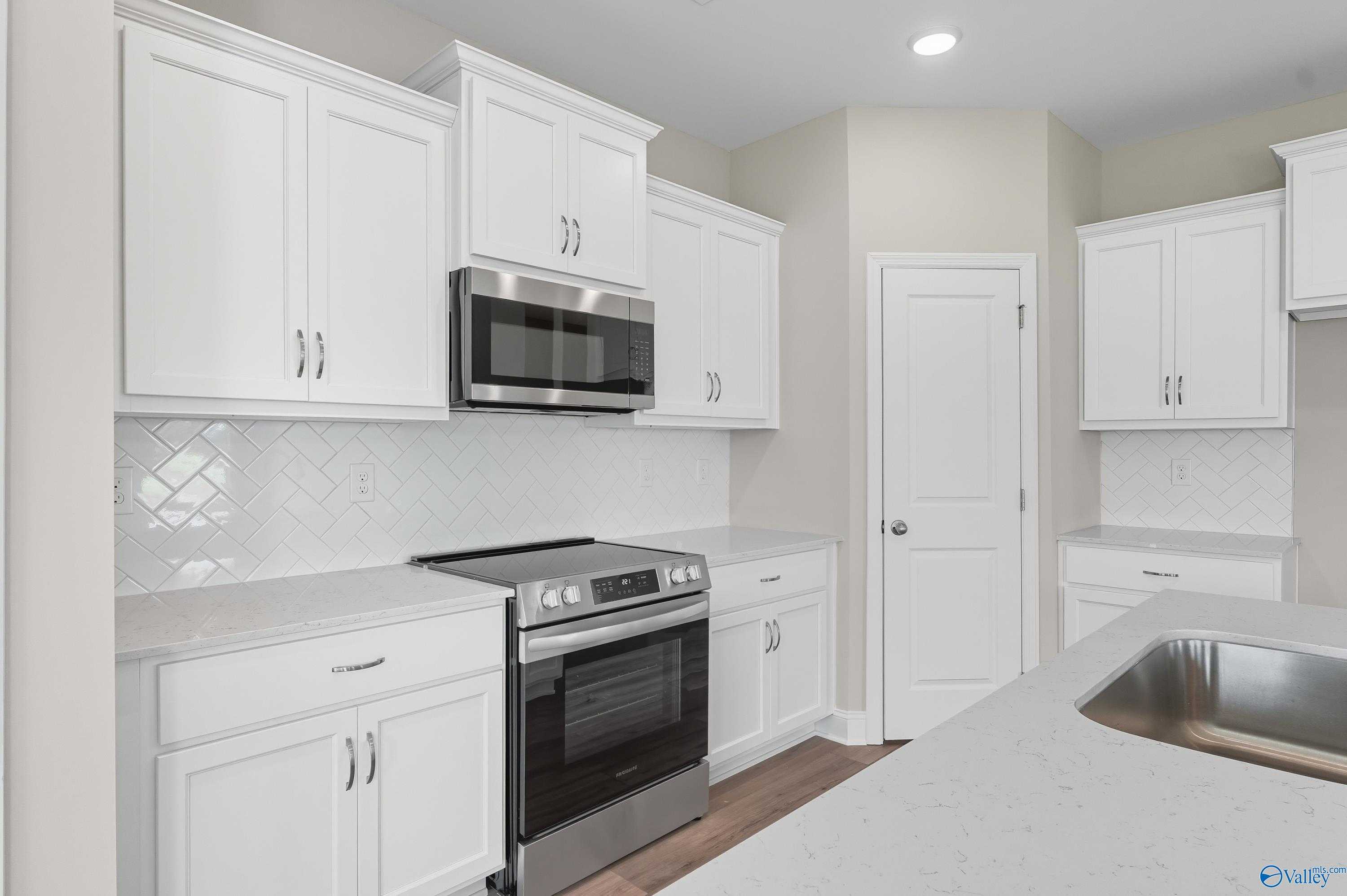 Modern white kitchen with stainless steel oven, microwave, subway tile backsplash in Davidson Homes The Franklin, Meridianville AL