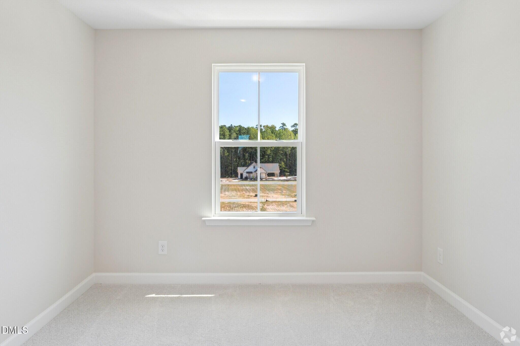 Bright carpeted bedroom with white walls and window overlooking trees in Davidson Homes The Mitchell plan, Knightdale NC