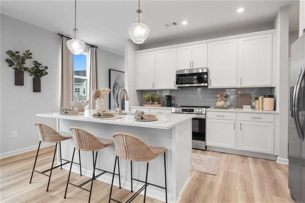 Modern open-concept kitchen with white cabinets, stainless appliances, and island bar seating in Davidson Homes Wilmington B, Emerson, GA