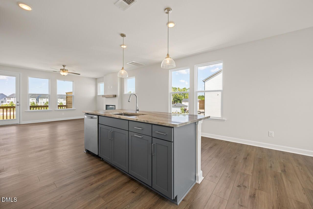 Open-concept kitchen with gray island, quartz countertops, pendant lights, and luxury vinyl plank flooring in Davidson Homes' Mitchell floor plan