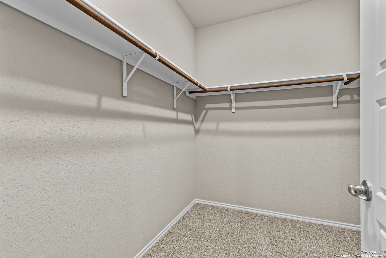 Spacious walk-in closet with white shelving, wooden rods, beige walls in Davidson Homes The Douglas F, San Antonio