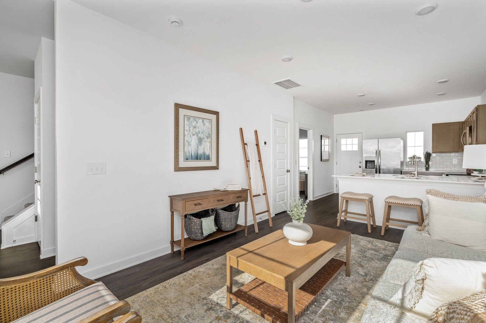Modern living room with gray sofa, wooden coffee table, ladder shelf, and open white kitchen in Davidson Homes Cumberland A, Gallatin, TN