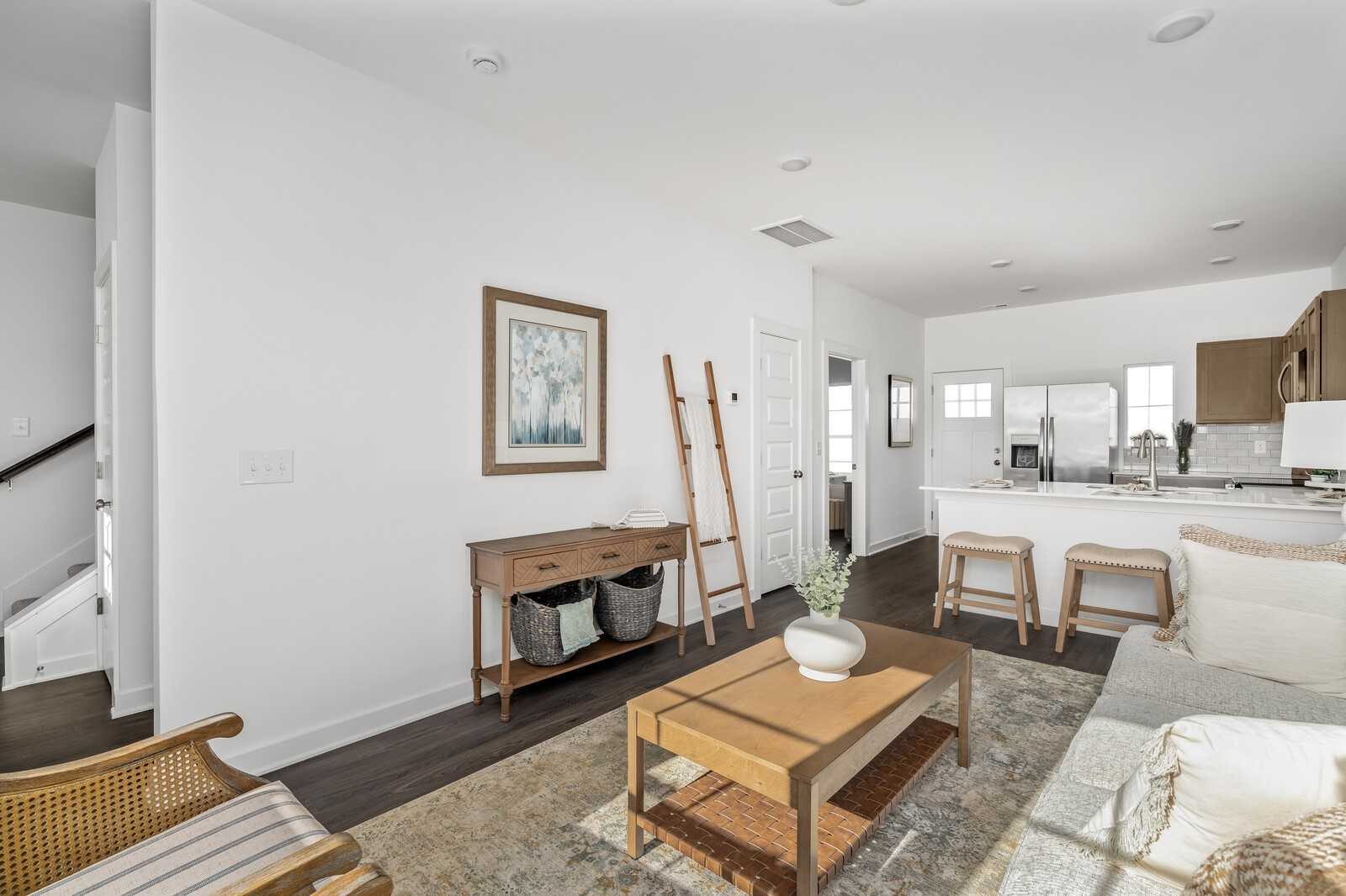 Modern living room with gray sofa, wooden coffee table, ladder shelf, and open white kitchen in Davidson Homes Cumberland A, Gallatin, TN
