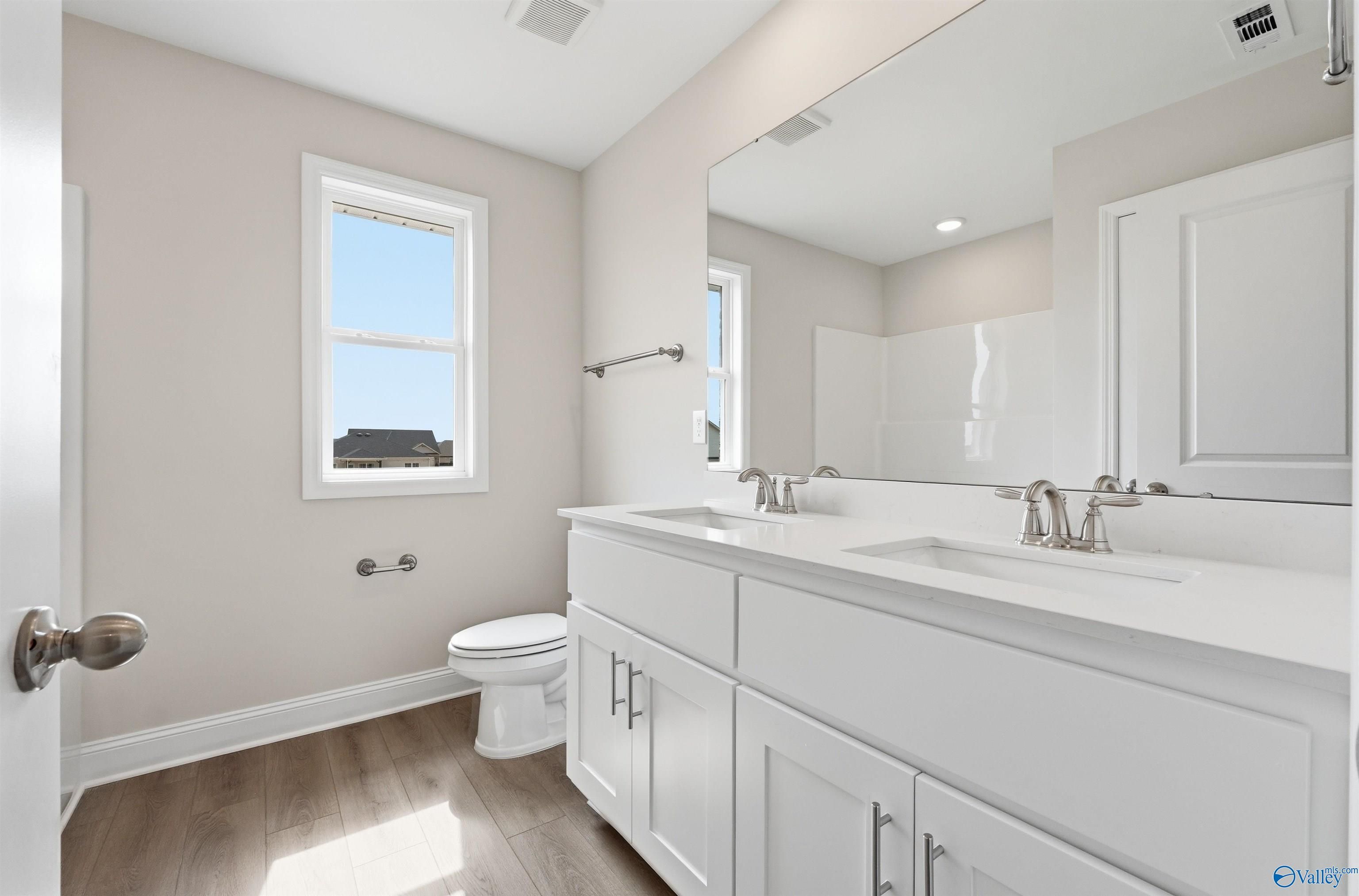 Modern bathroom with dual vanity, white cabinetry, and wood-look flooring in The Shelby D home, Evergreen Mill, Madison, AL.