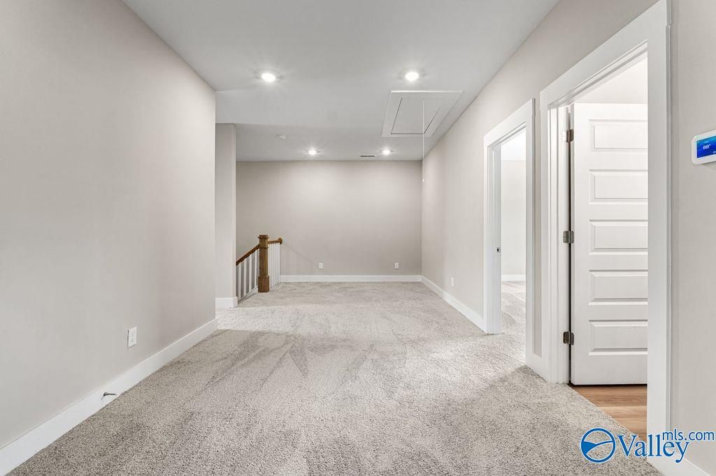 Spacious upstairs hallway with gray carpet, white doors, and wooden staircase in Evermore Homes The Oxford, Owens Cross Roads, Alabama