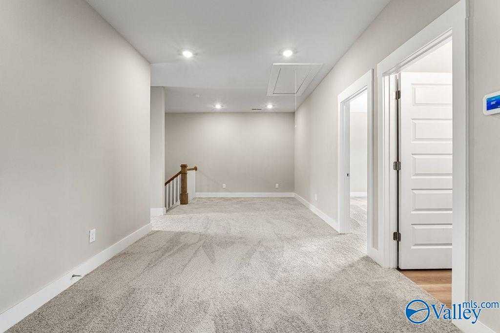 Spacious upstairs hallway with gray carpet, white doors, and wooden staircase in Evermore Homes The Oxford, Owens Cross Roads, Alabama