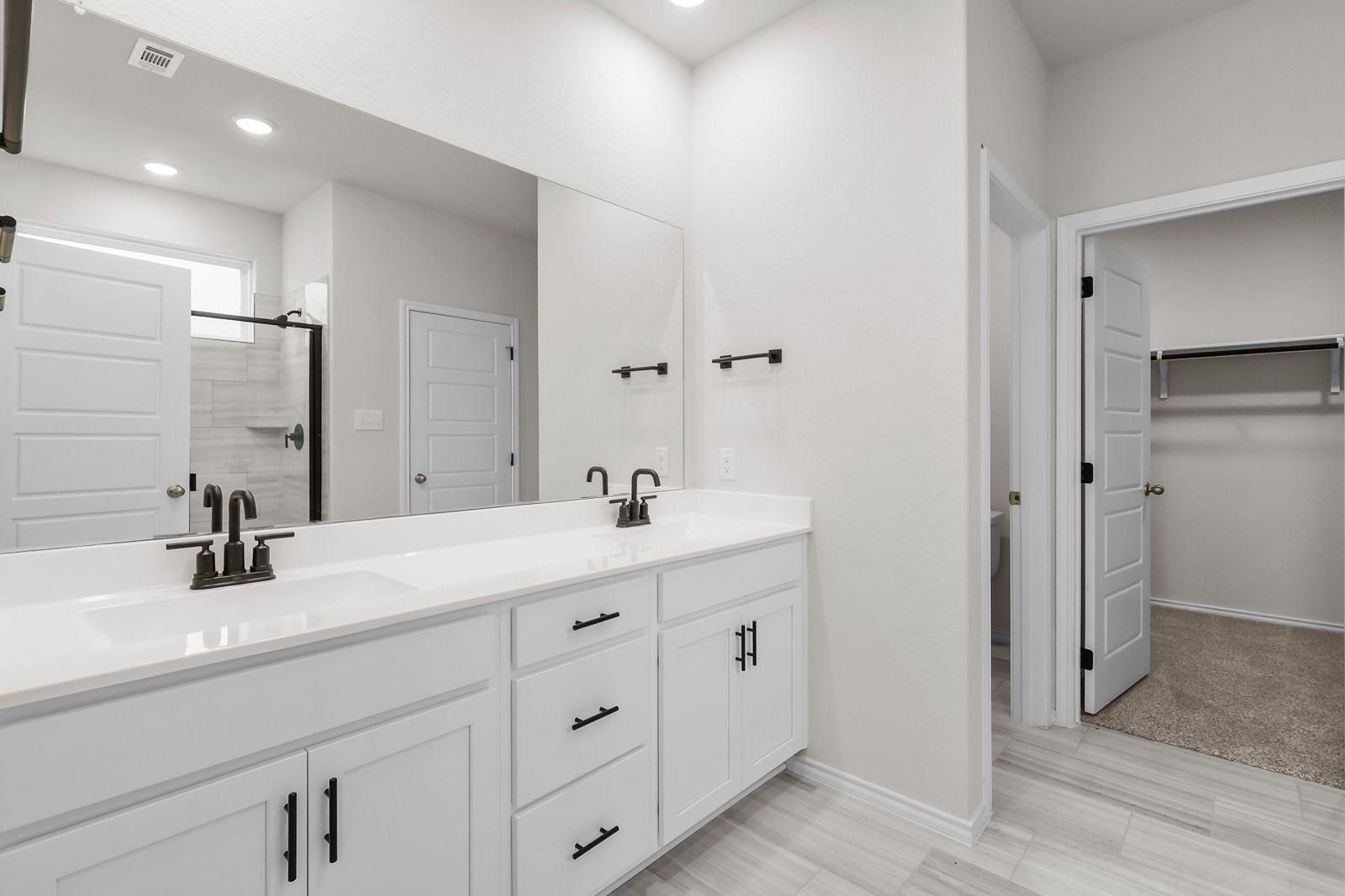 Modern primary bathroom in The Sequoia C featuring white dual-sink vanity, matte black fixtures, and walk-in closet.