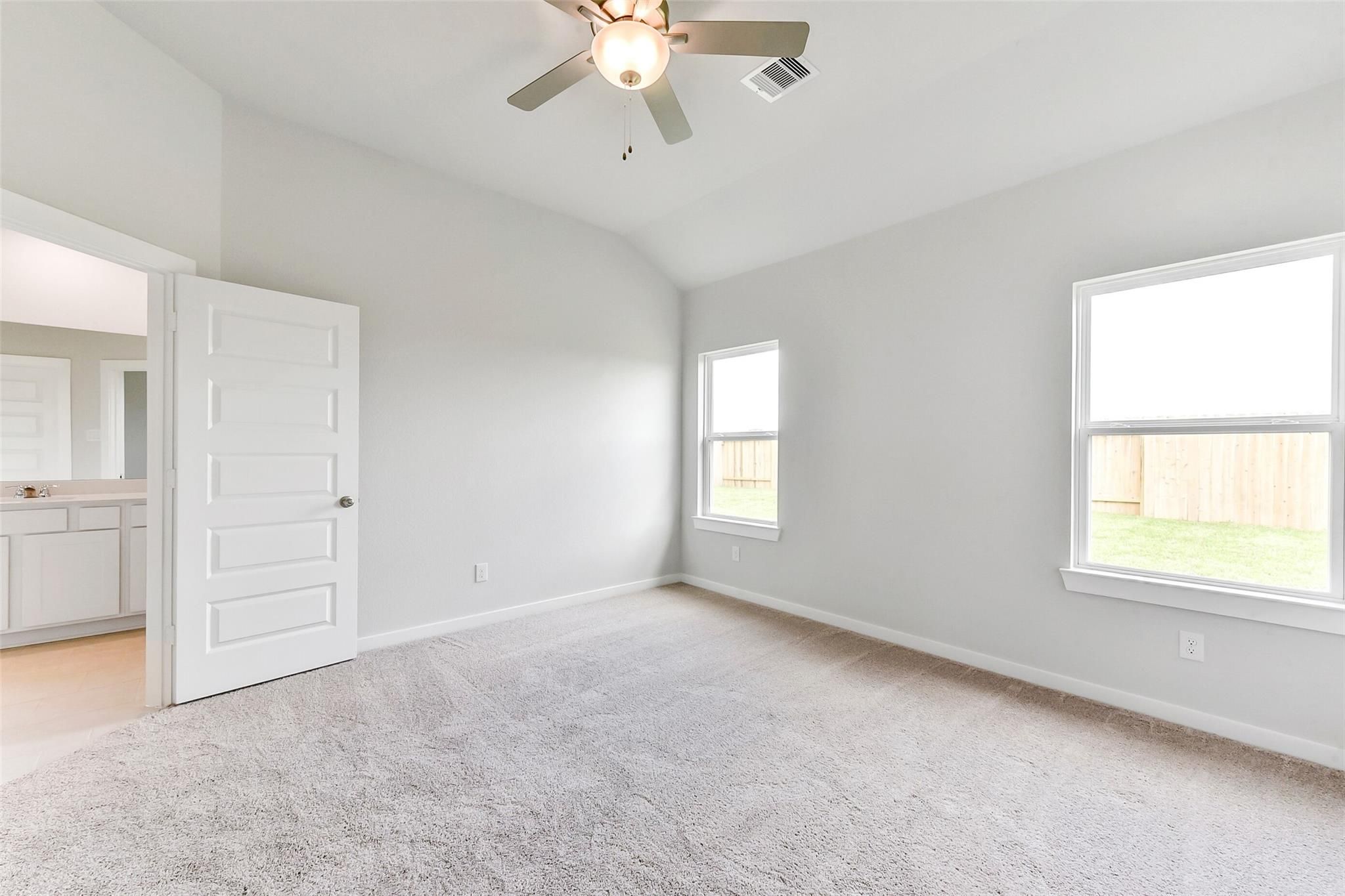 Bright bedroom with ceiling fan, carpet floor, large windows, and en-suite bath in Davidson Homes The Costa B, Dayton, Texas
