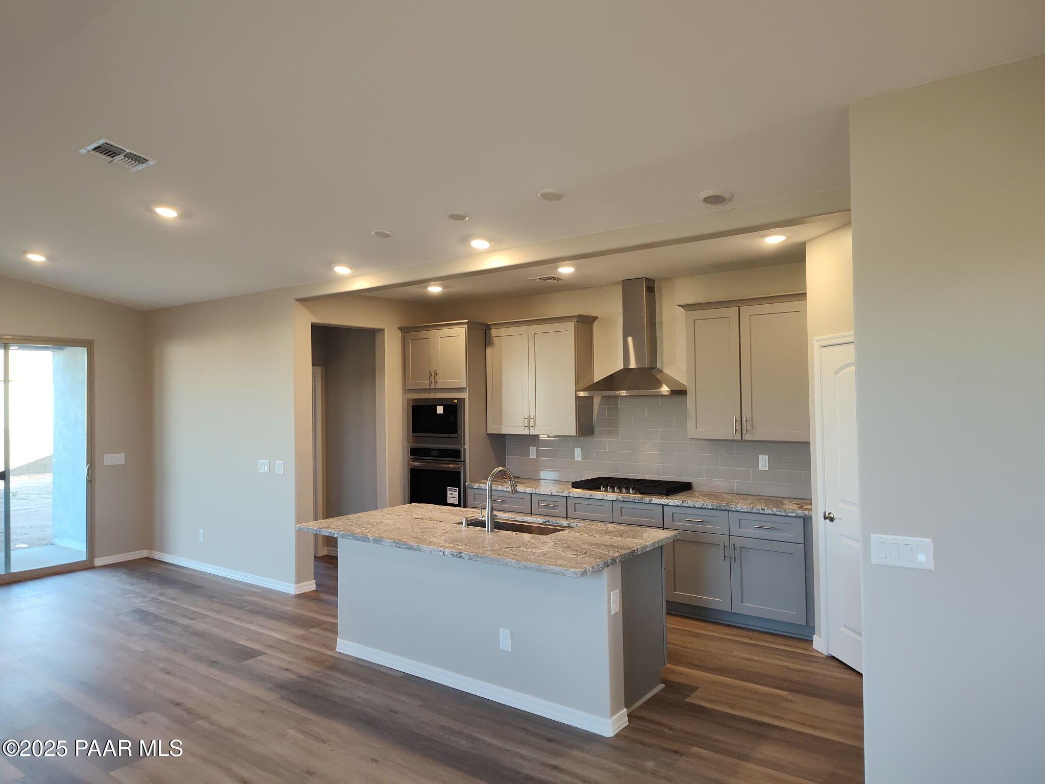 Modern kitchen featuring large island sink, stainless steel range hood, double oven, and white shaker cabinets in Davidson Homes The Frontier A, Prescott Valley, AZ