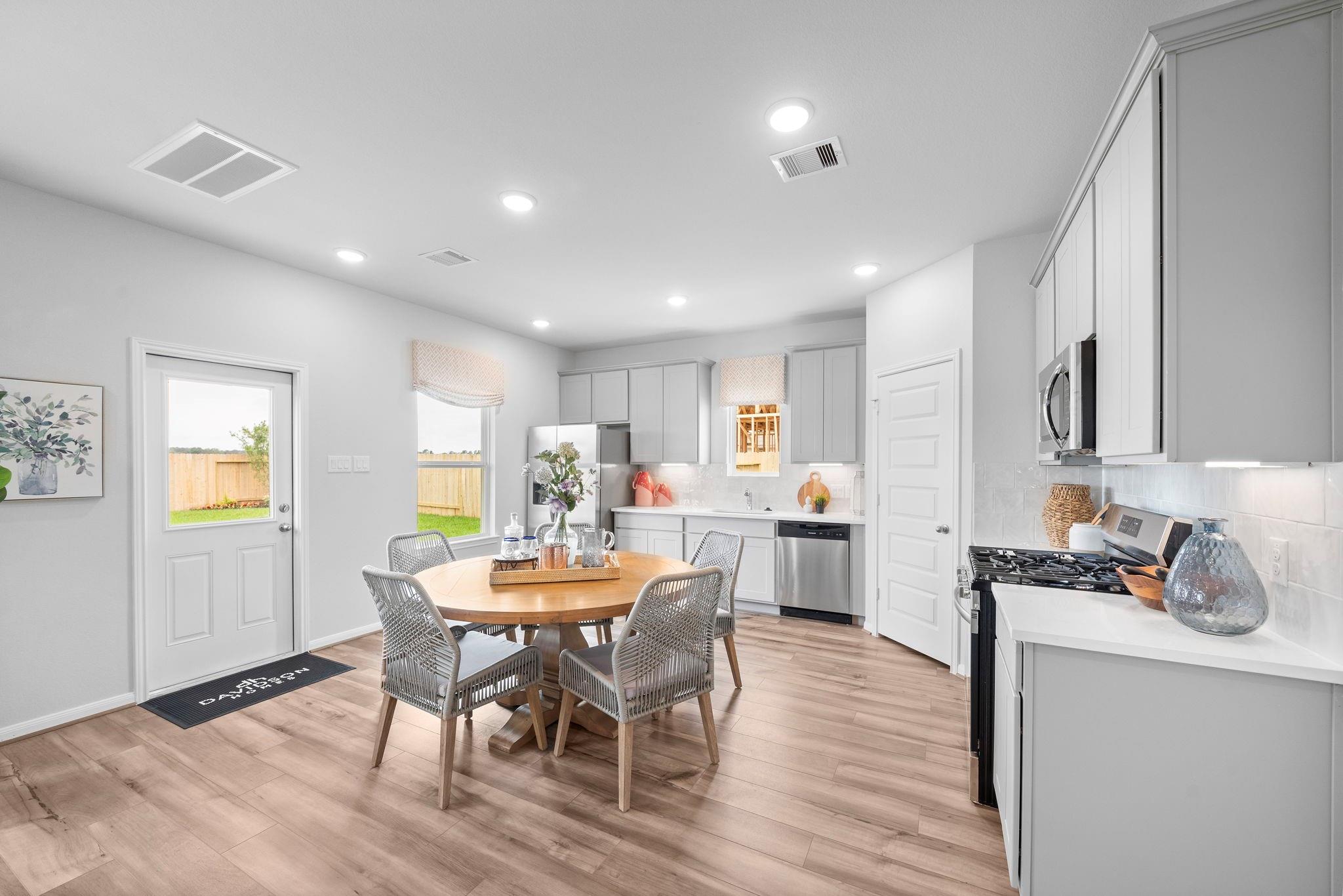 Bright open-concept kitchen and dining area with white cabinets, stainless appliances, and wood-look flooring in Davidson Homes' Trinity F plan, Splendora, TX