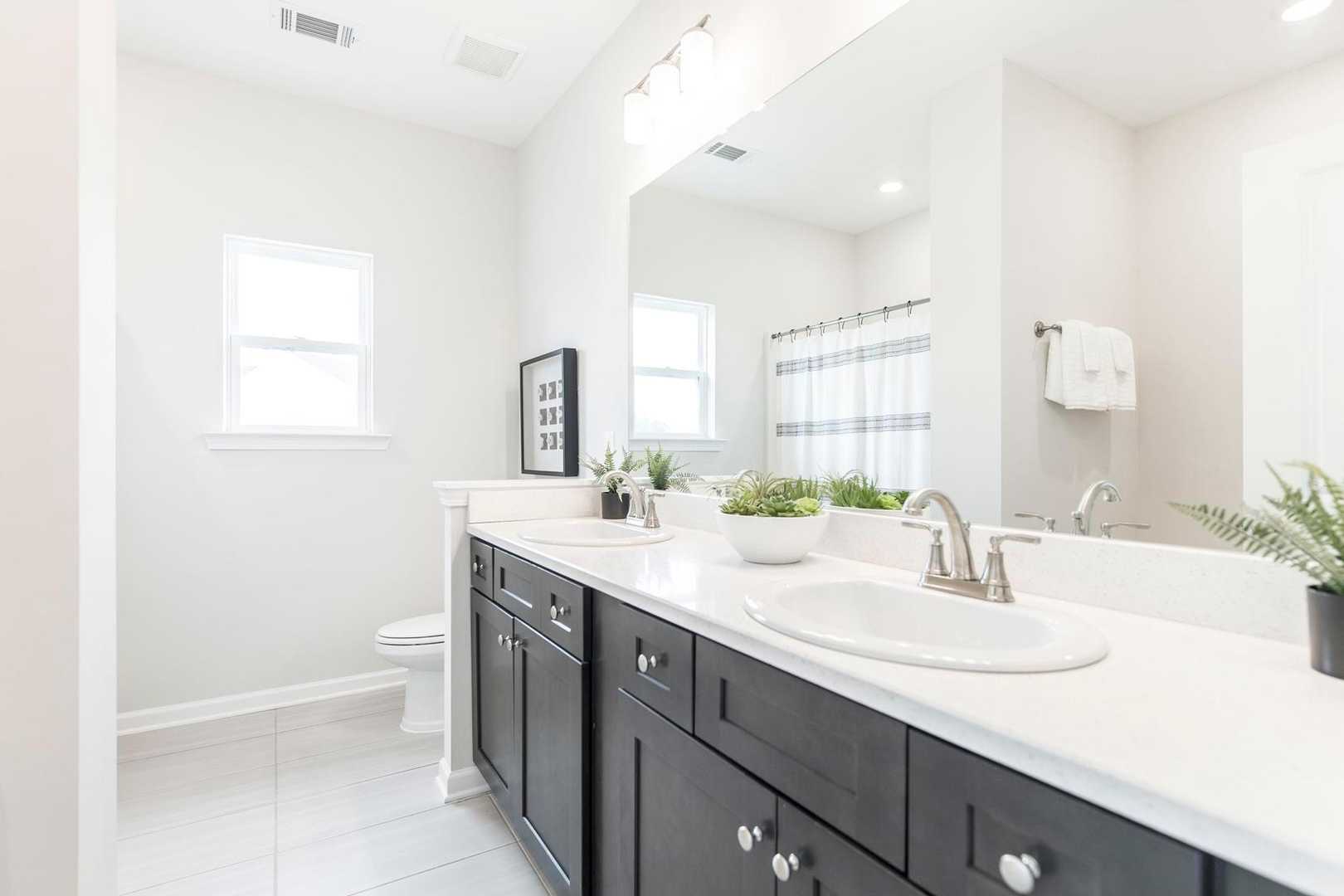 Spacious primary bathroom with double vanity, dark cabinets, and greenery at Cape Reserve Donahue Ridge in Auburn AL