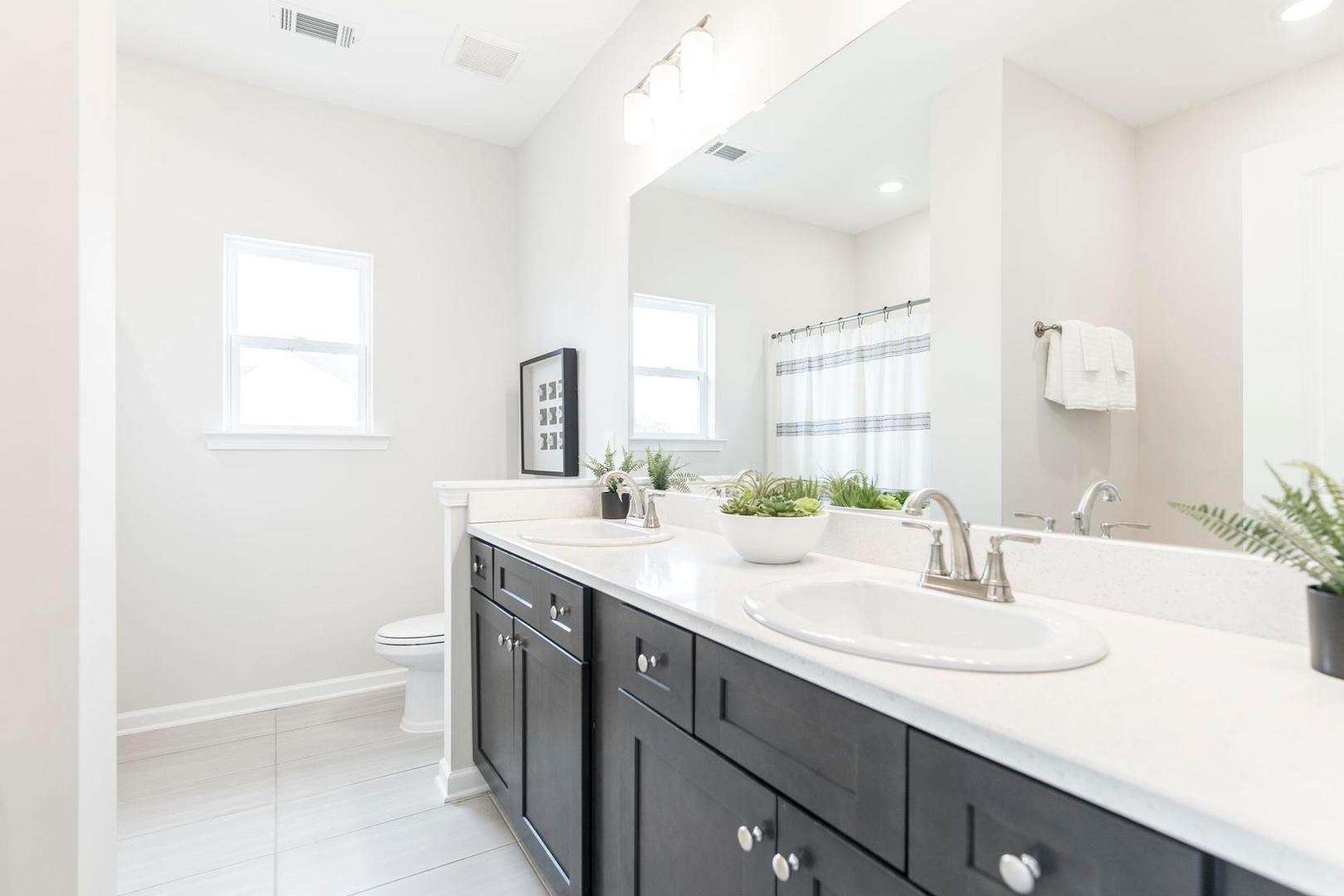 Spacious primary bathroom with double vanity, dark cabinets, and greenery at Cape Reserve Donahue Ridge in Auburn AL
