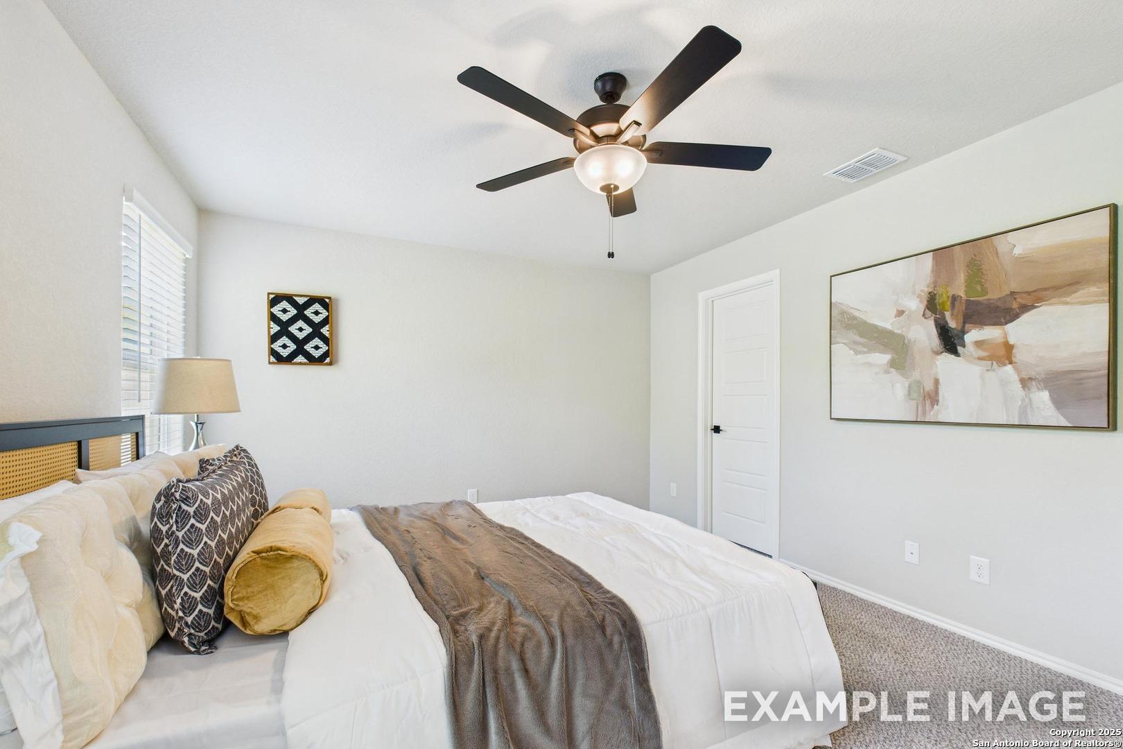 Cozy secondary bedroom with ceiling fan, abstract art, rattan headboard, and plush bedding in Davidson Homes The Charlotte B, San Antonio