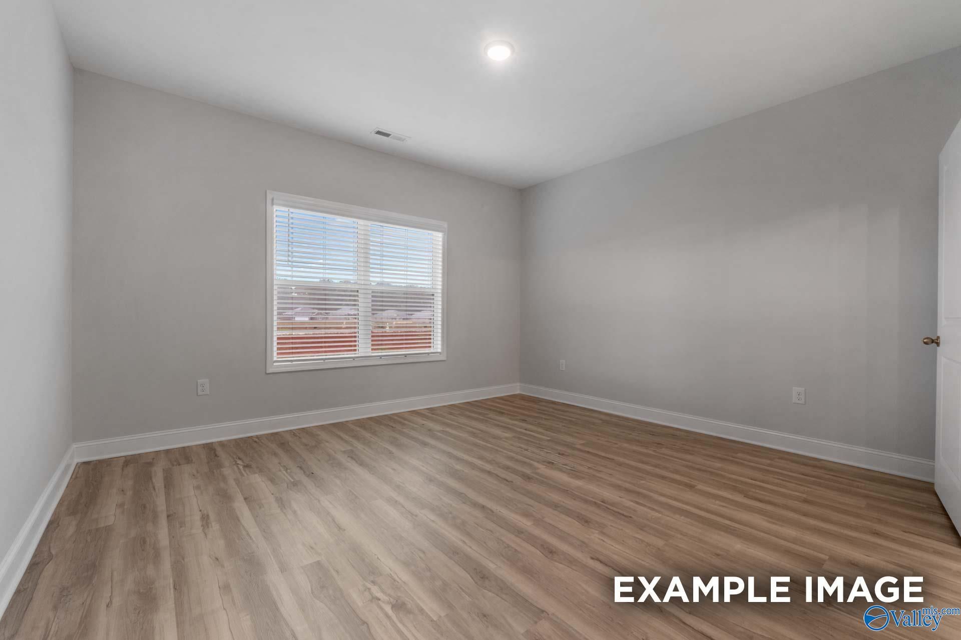 Bright secondary bedroom with light gray walls, hardwood floors, and large window in Davidson Homes The Cumberland B, Decatur, Alabama