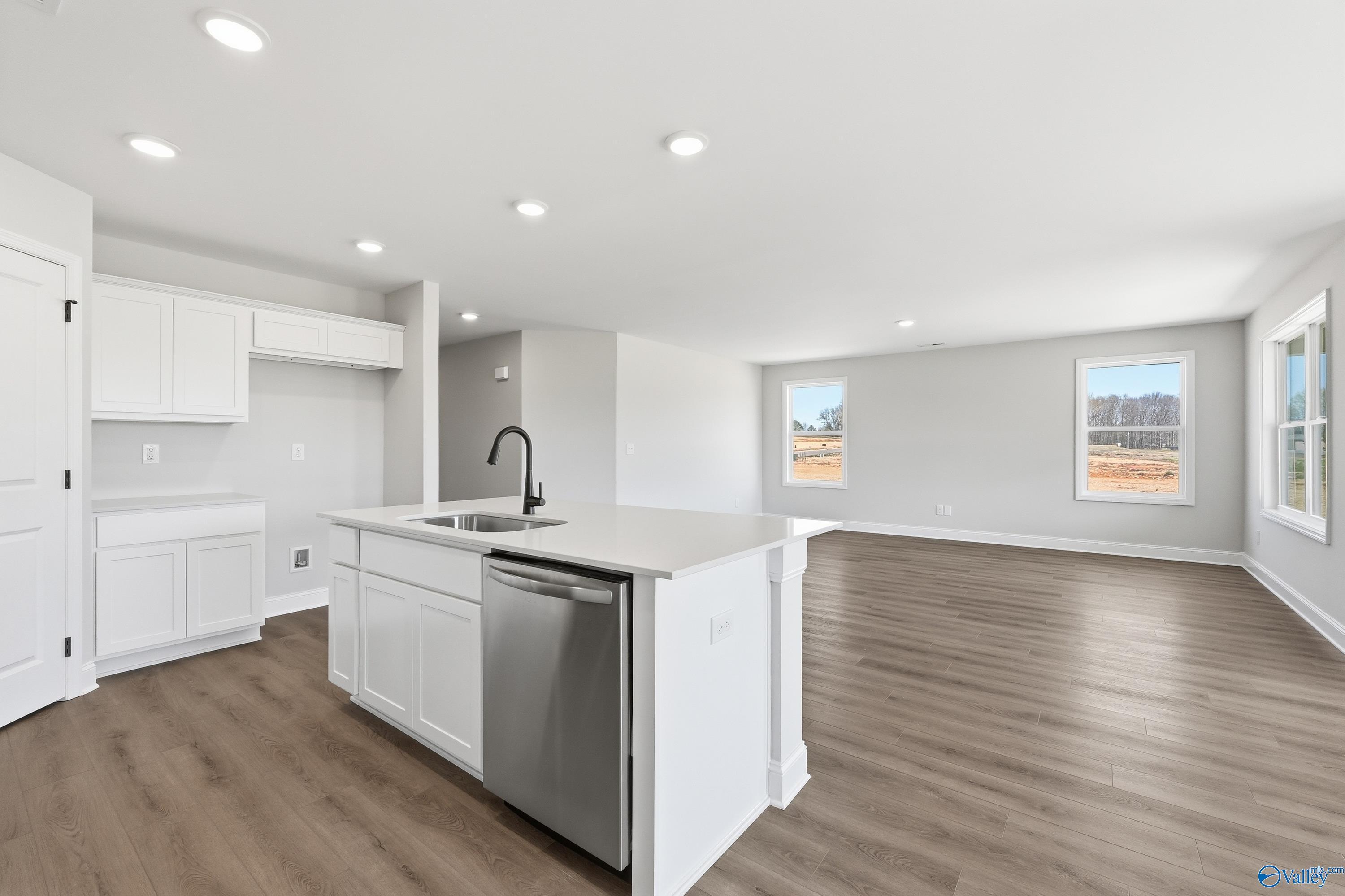 Open-concept kitchen with white cabinets, quartz island, farmhouse sink, stainless dishwasher in The Franklin V by Davidson Homes, Athens AL